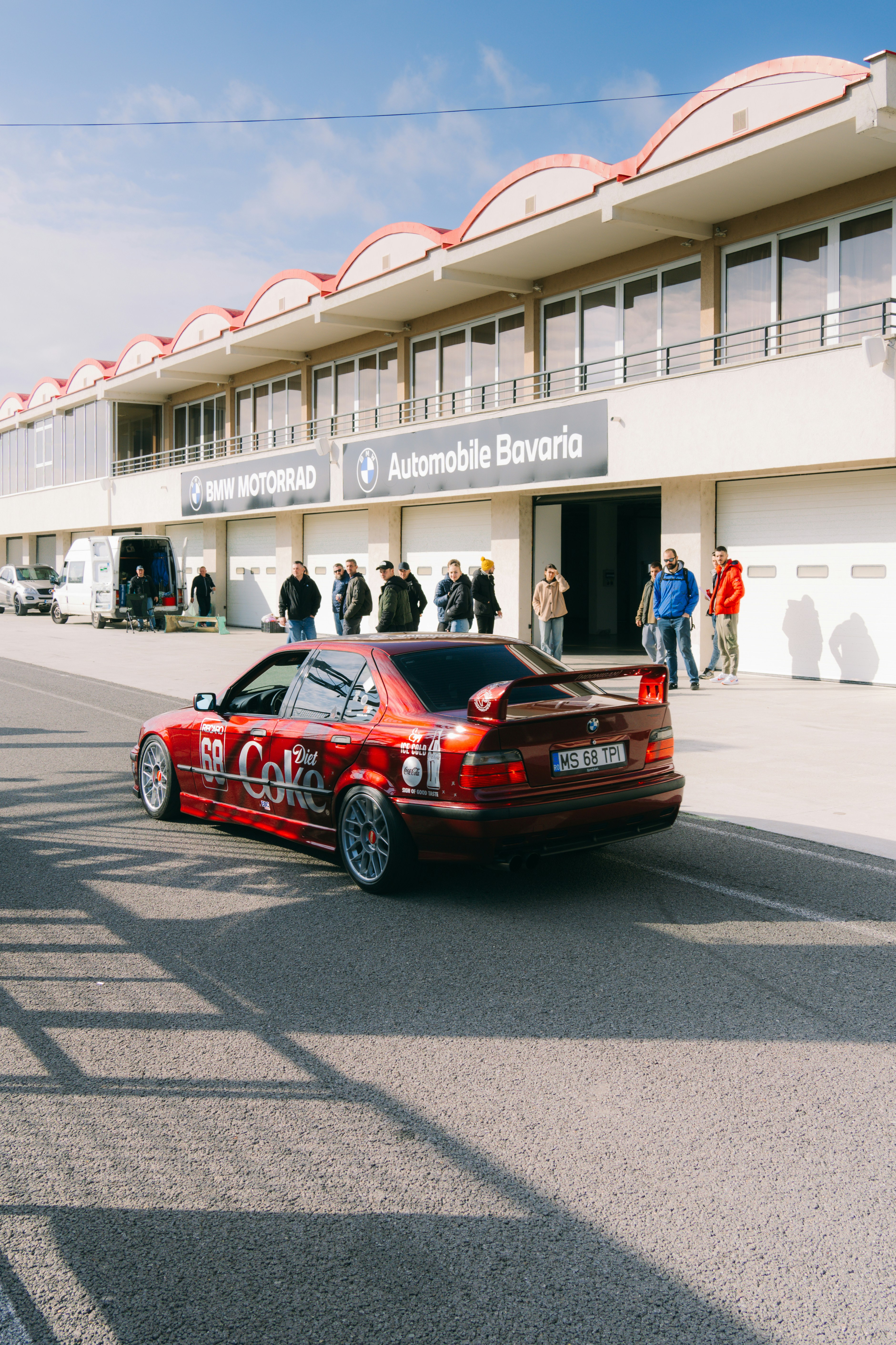 A red car driving down a street next to a tall building