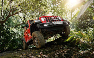A red jeep driving through a forest on a trail
