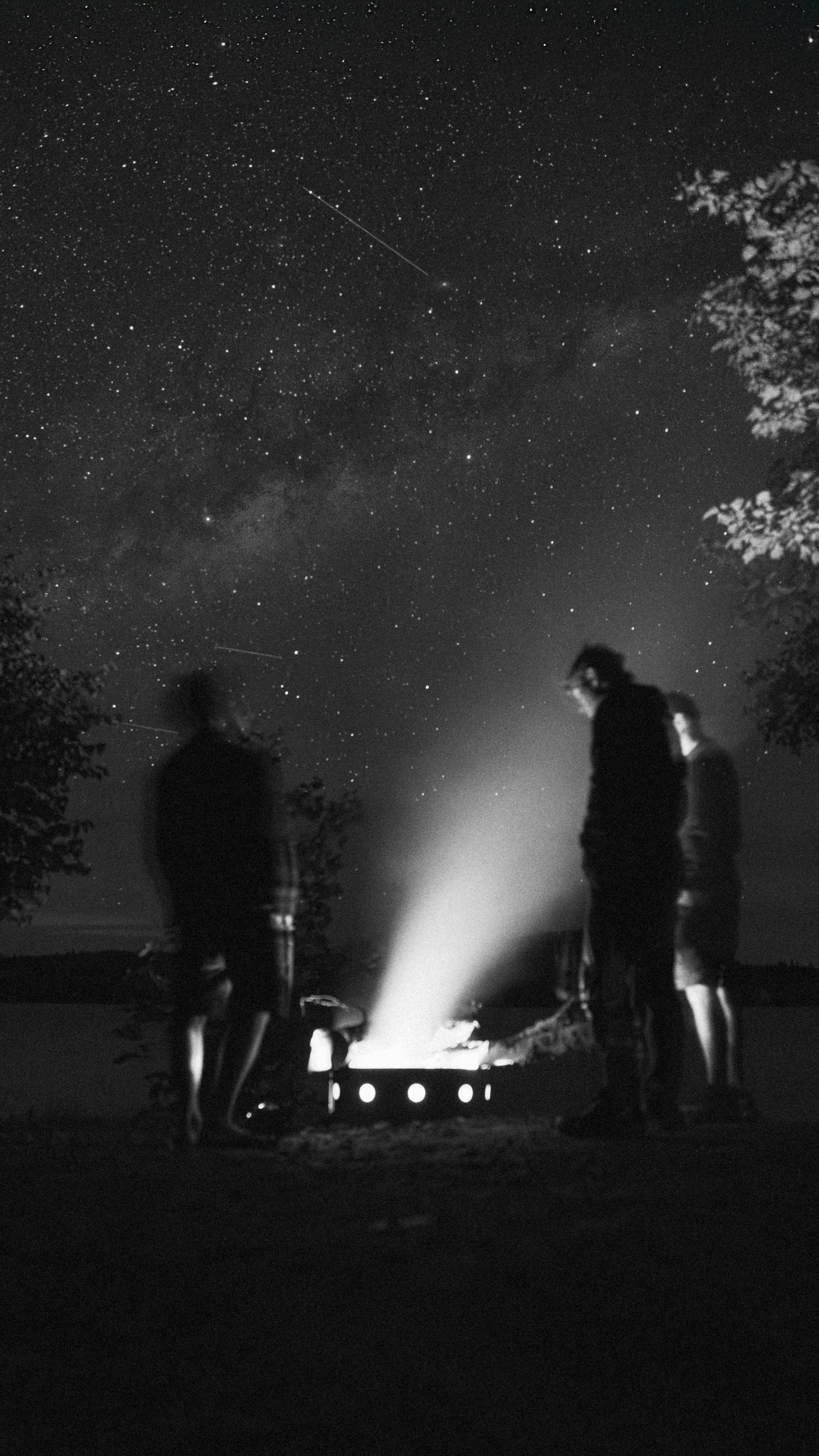 Three people standing around a campfire under a night sky