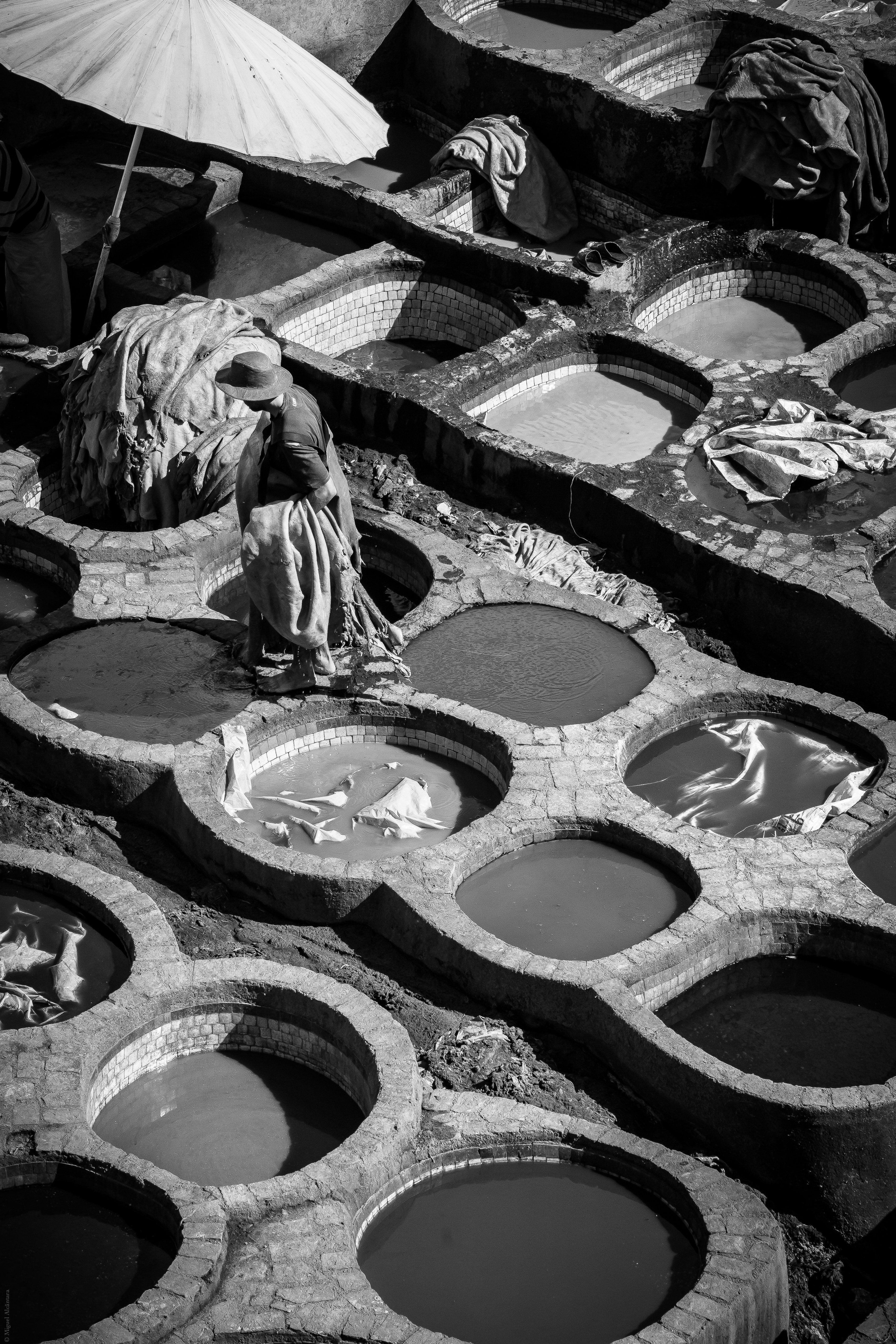 Curtume tradicional a céu aberto, em preto e branco, com tanques e trabalhadores