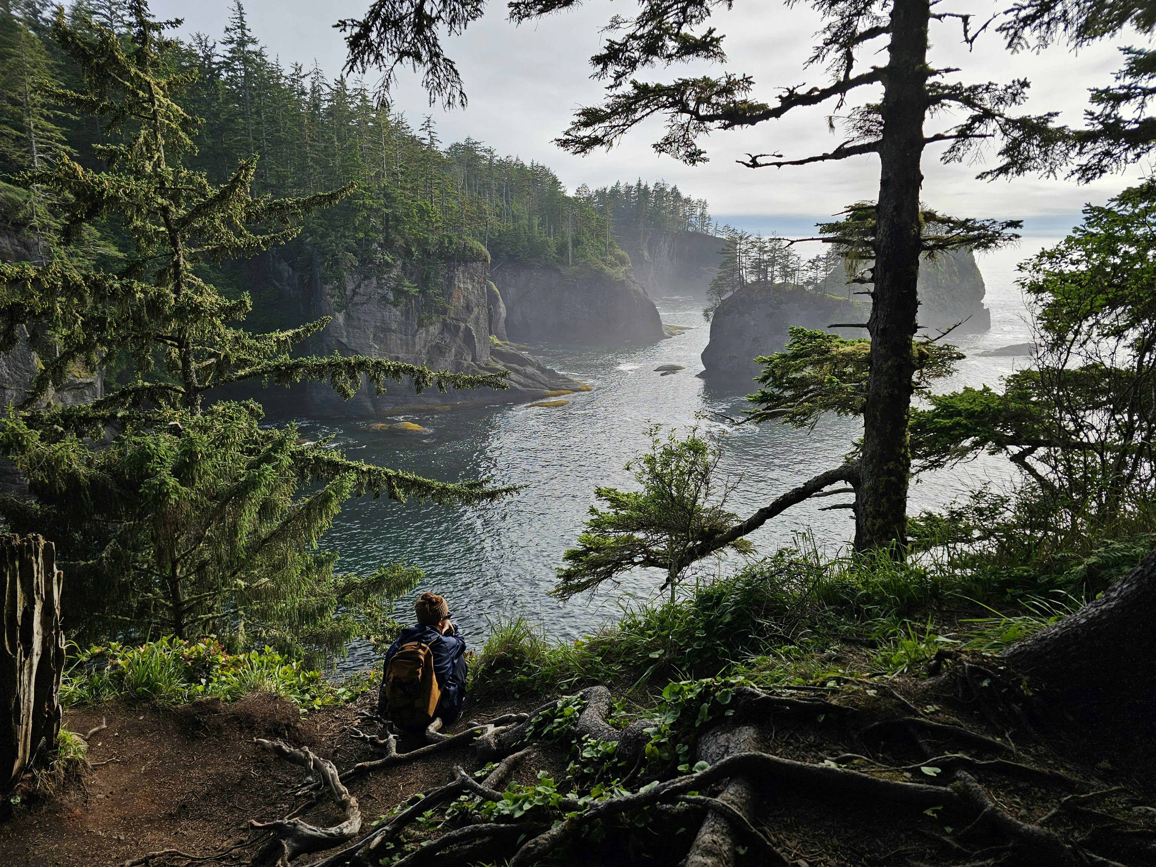 A person is sitting on a trail overlooking the water