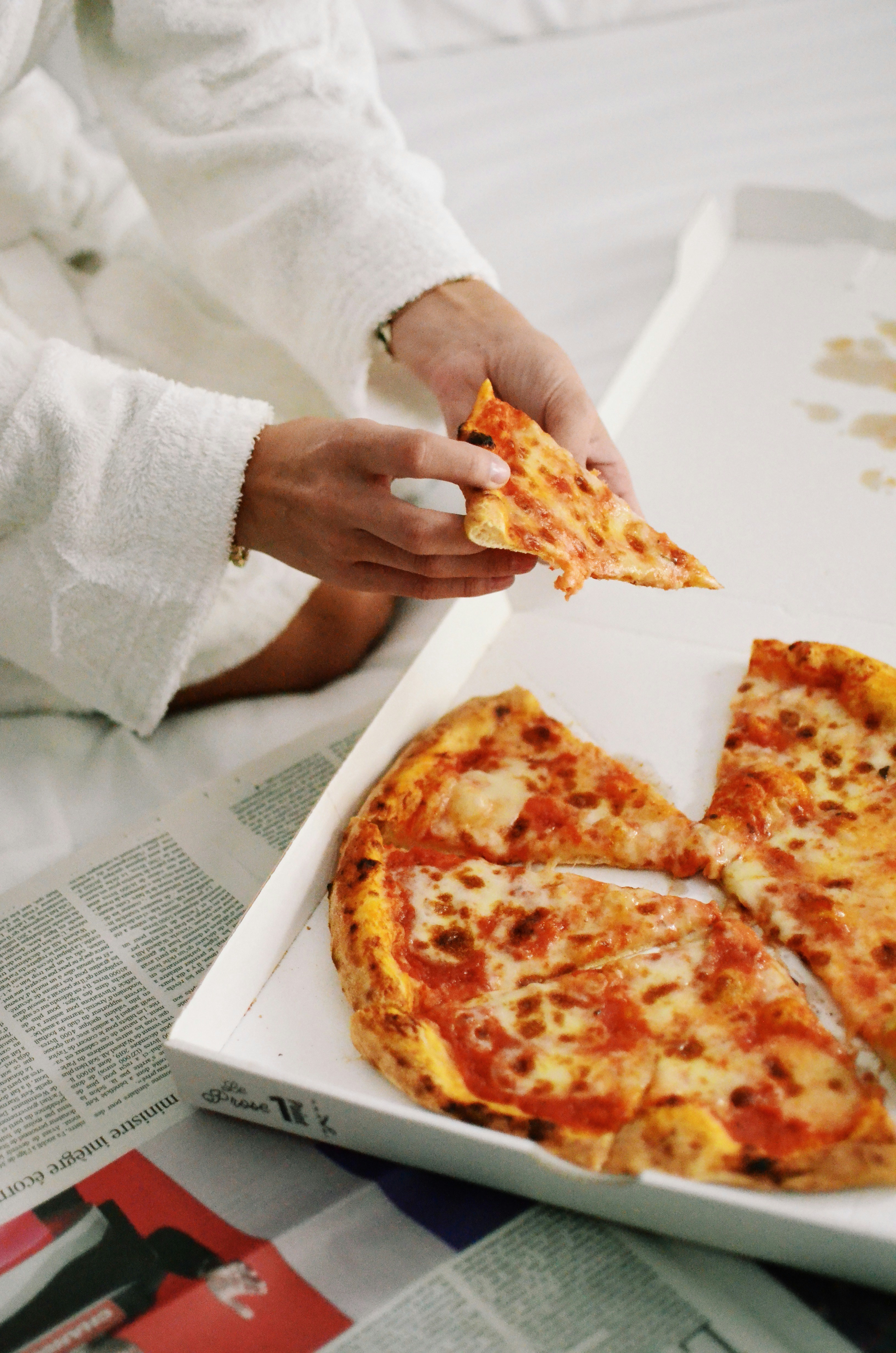 A person holding a slice of pizza in a box