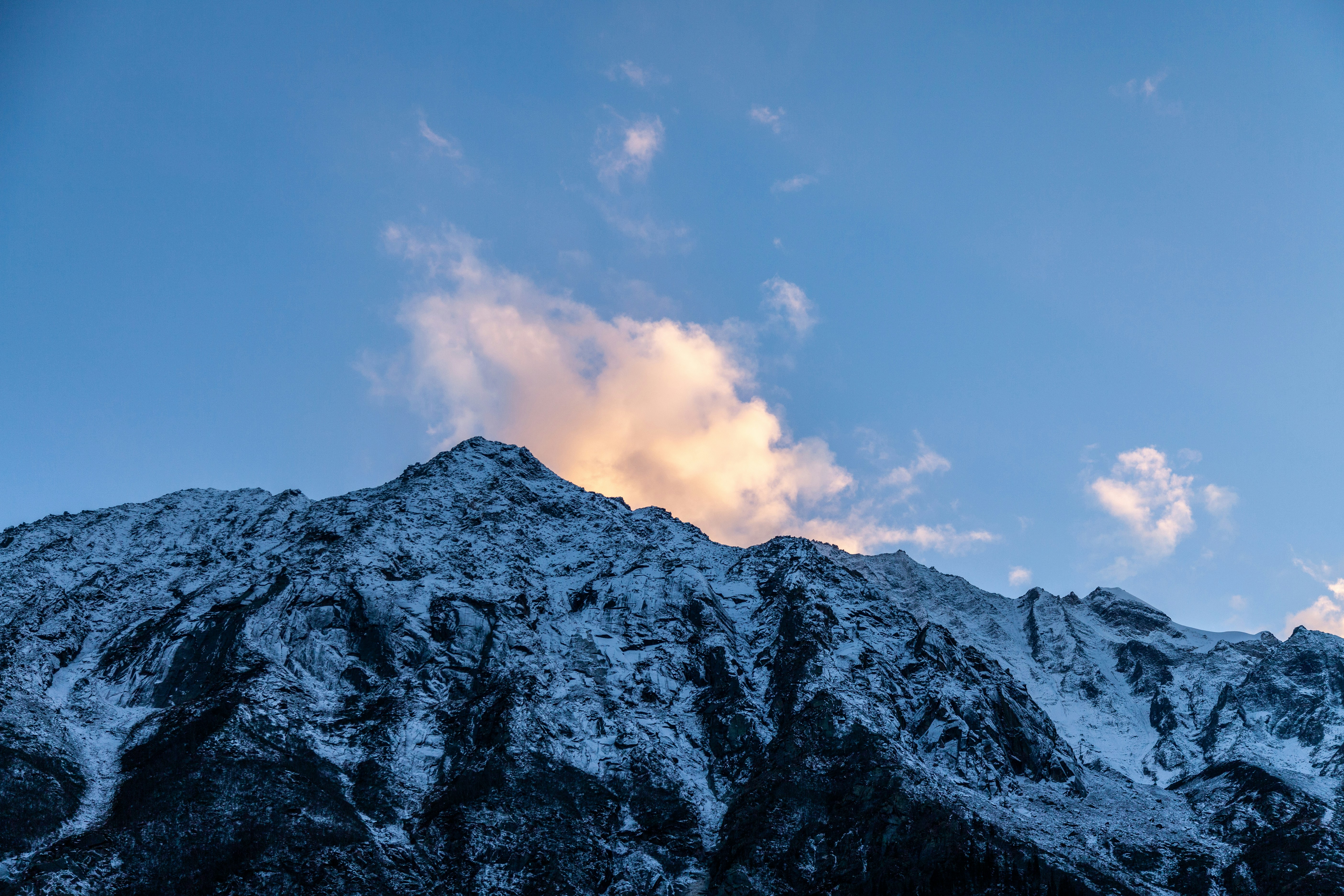 A snow covered mountain under a cloudy blue sky