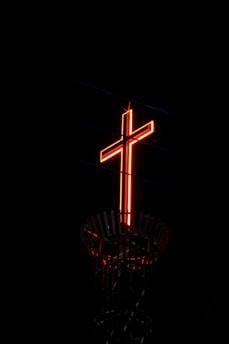 A cross on top of a tower lit up in the dark