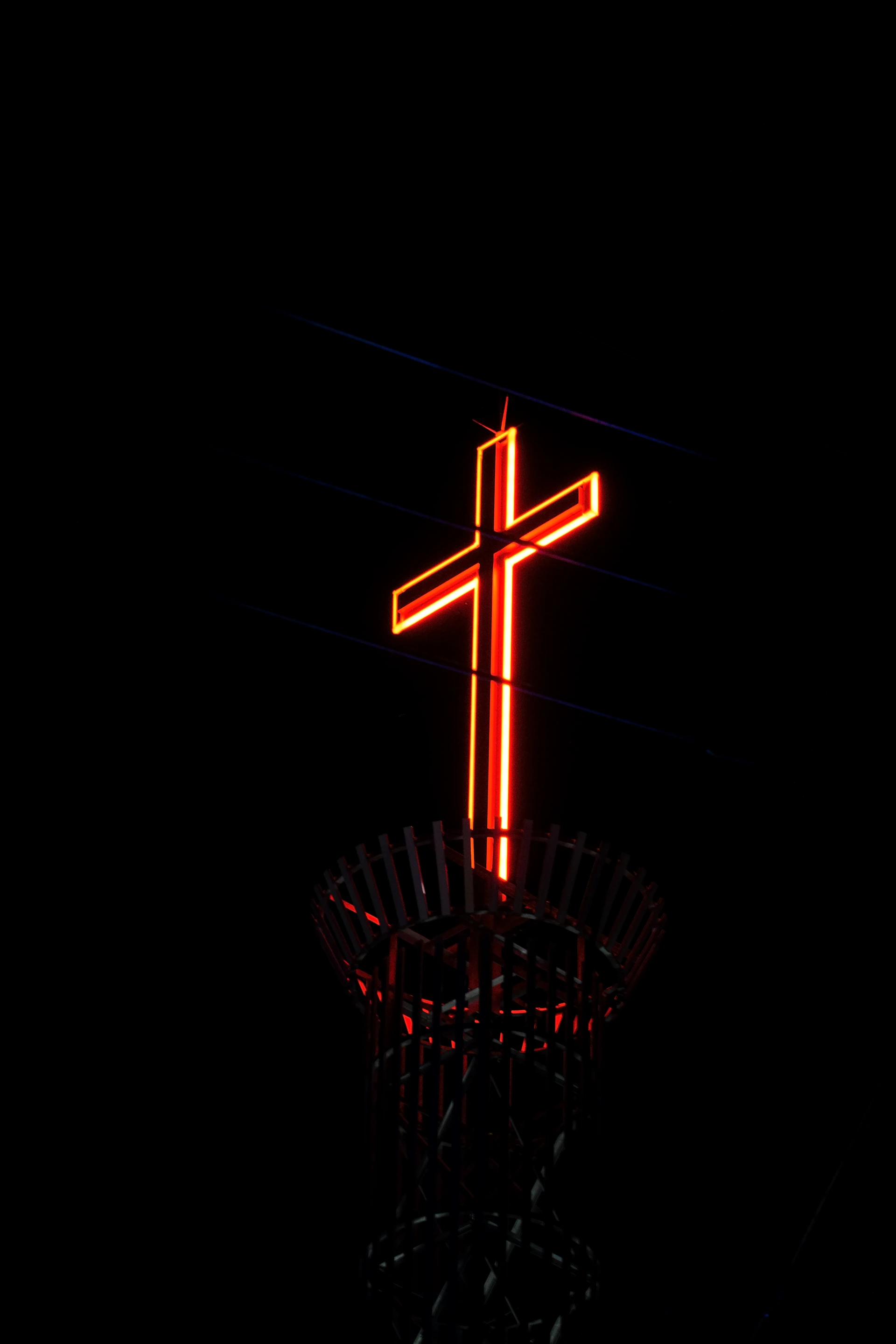 A cross on top of a tower lit up in the dark