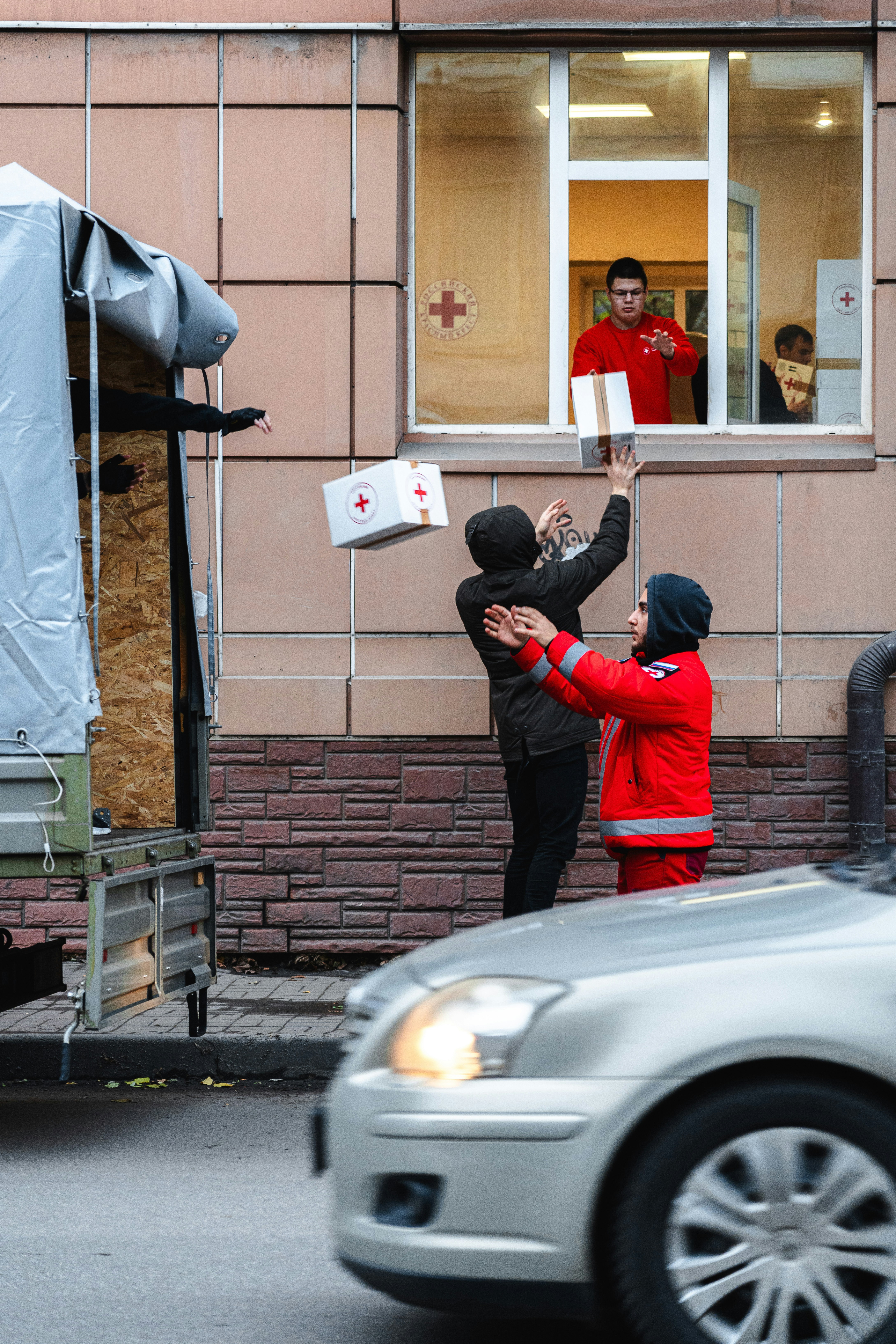People pass aid boxes from building window to street truck.
