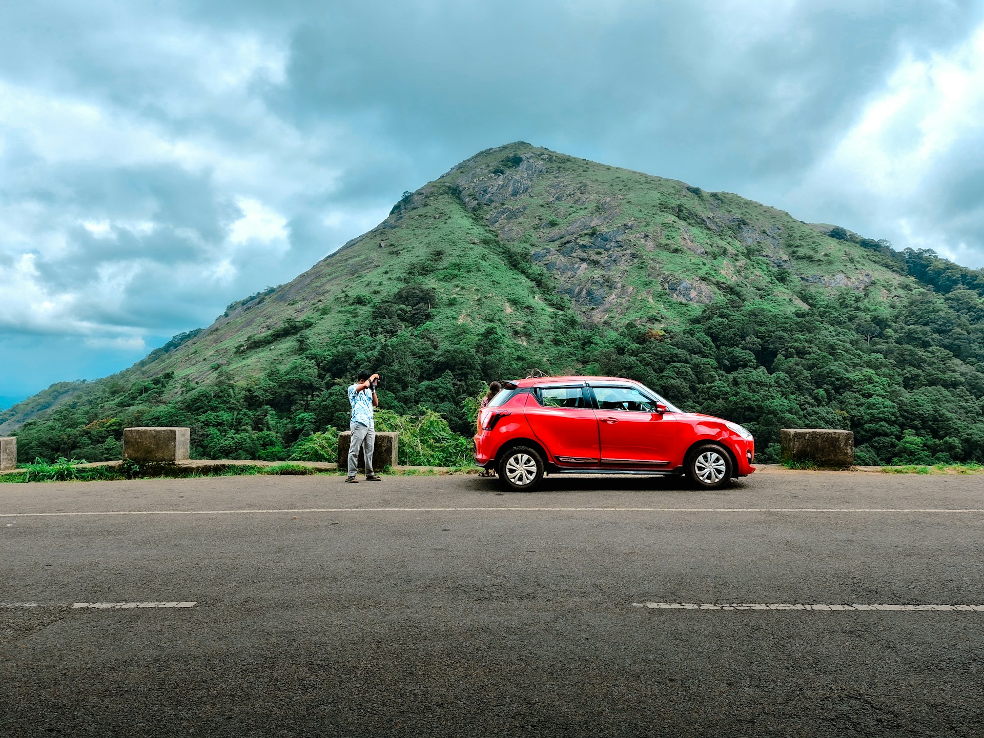 A man standing next to a red car in front of a mountain