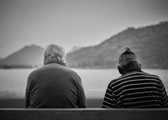 Two people sitting on a bench looking at the water