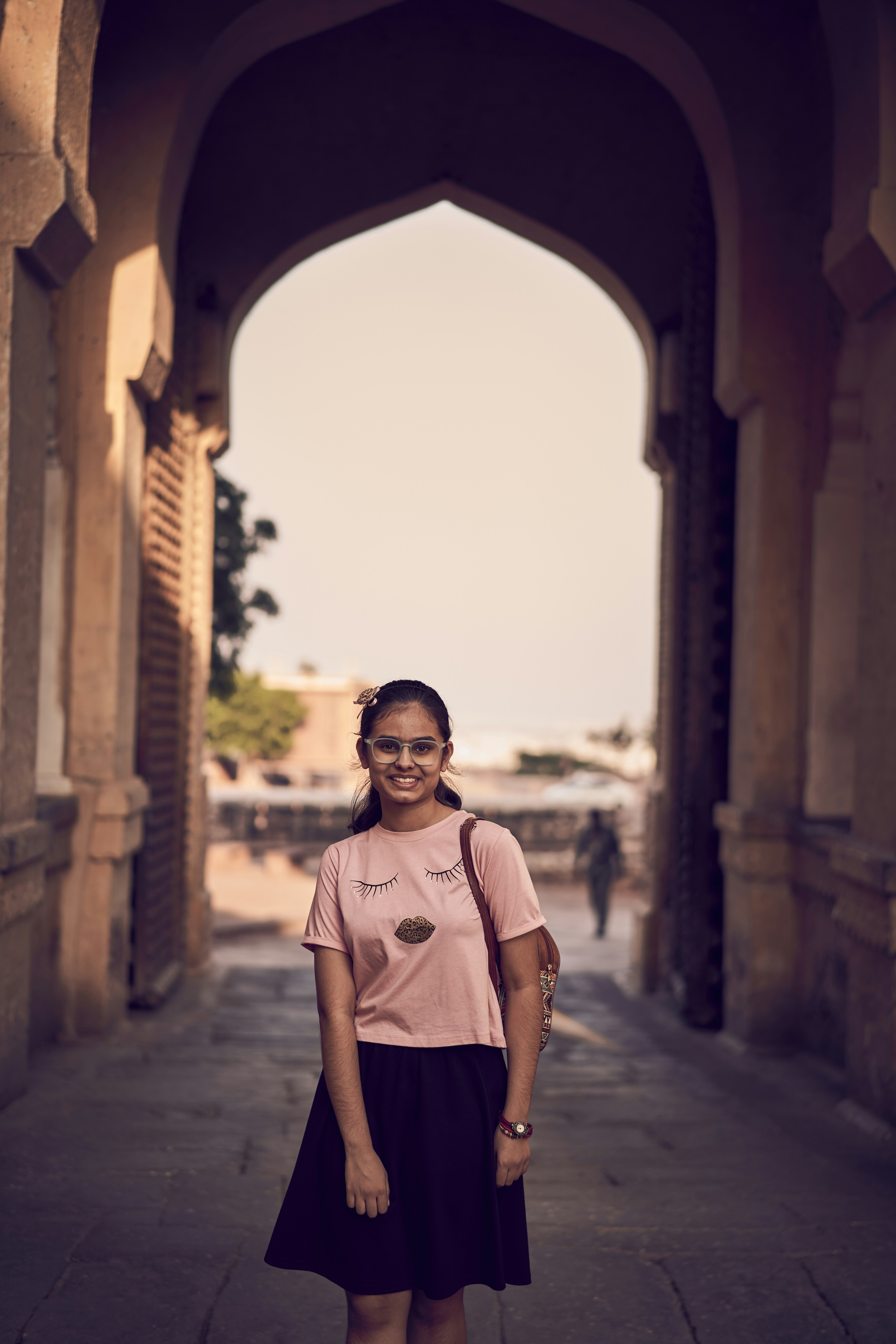 A woman standing on a sidewalk in front of an archway