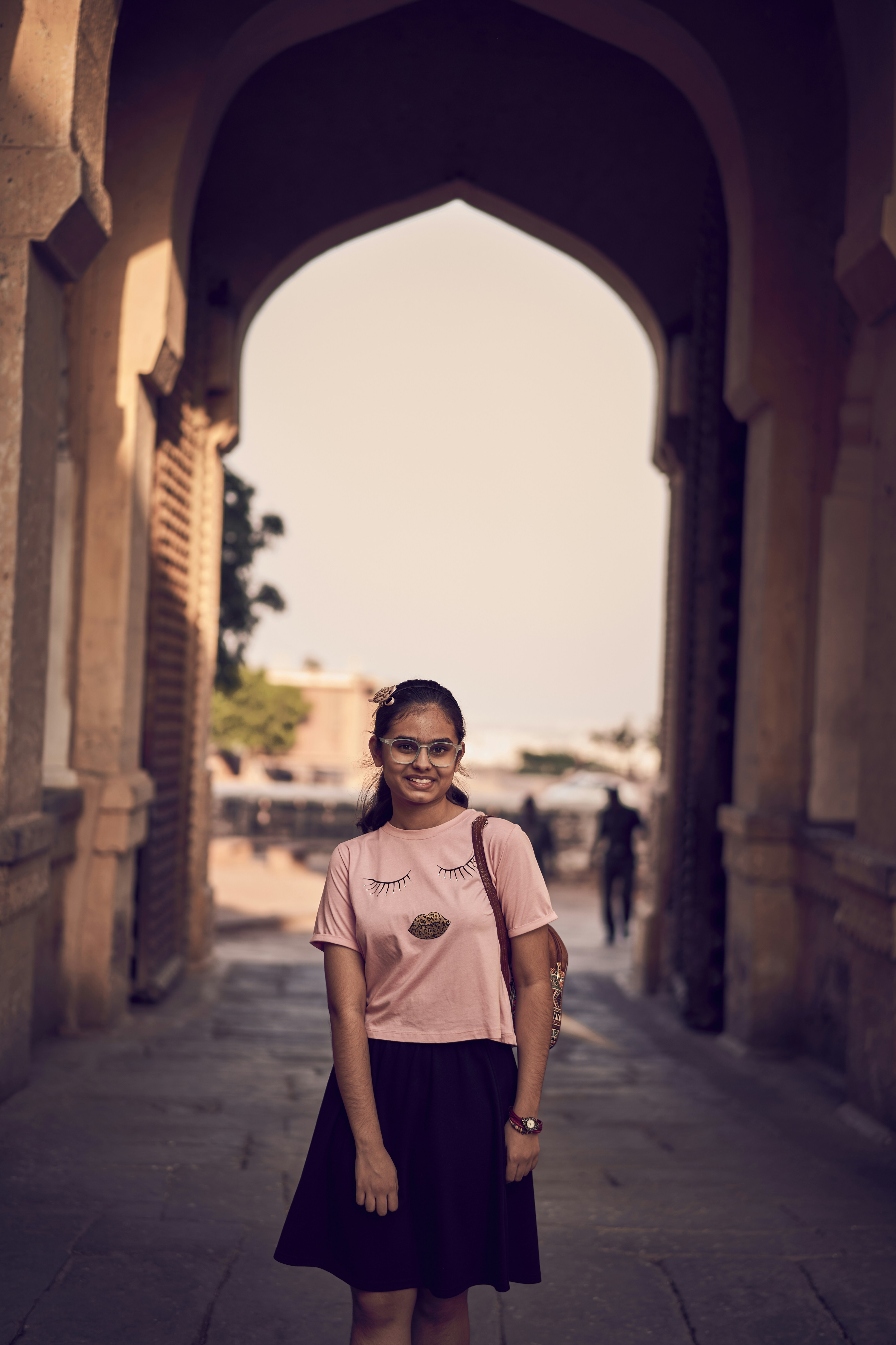A woman in a pink shirt and black skirt standing in an archway