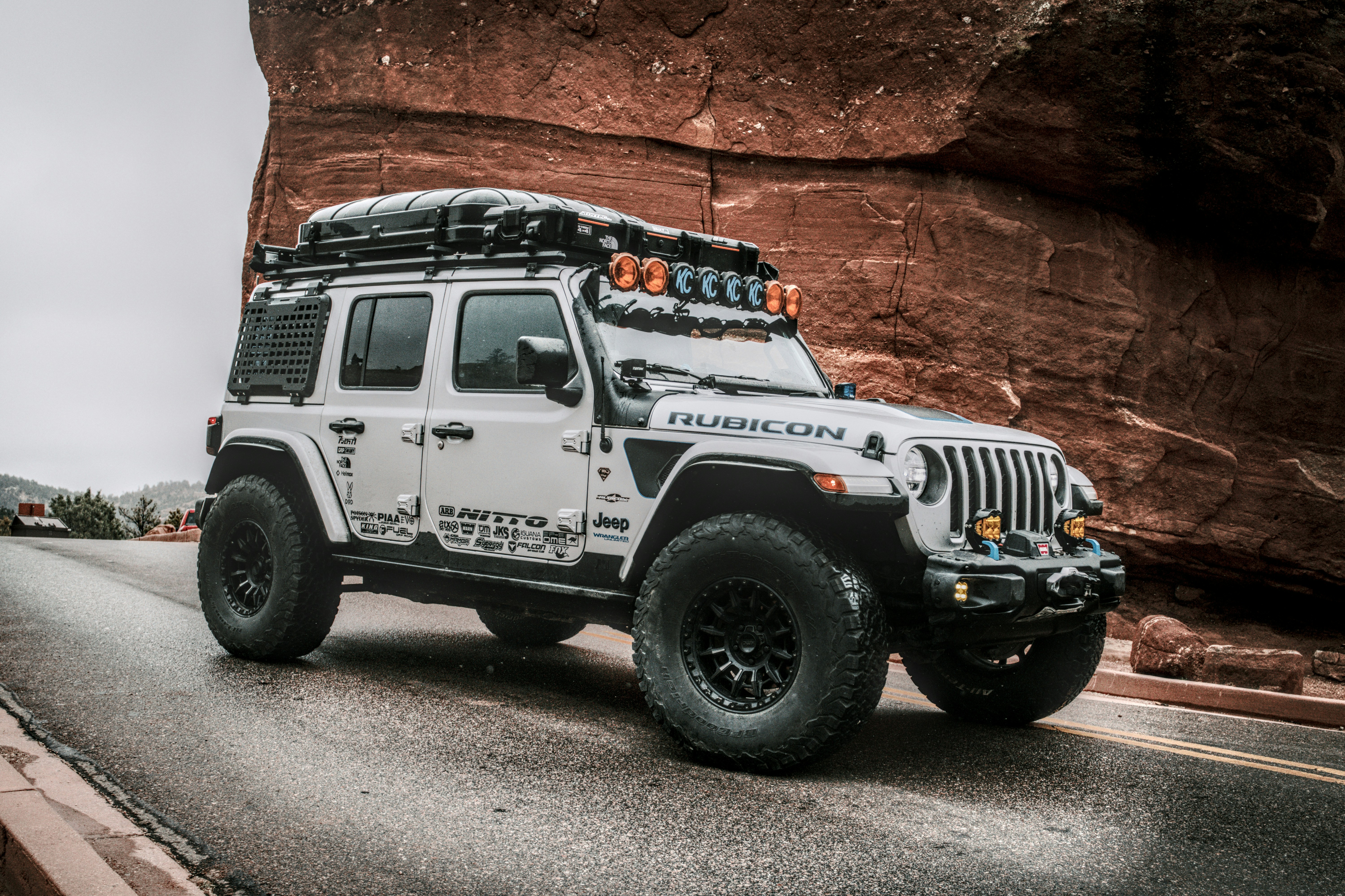 하얀 지프 한 대가 큰 바위 옆 도로를 달리고 있다