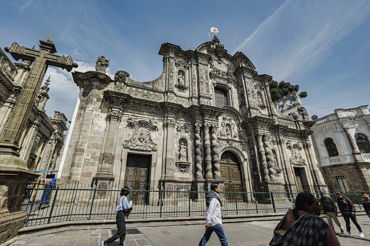 People walking past a carved stone church front in Quito's old town