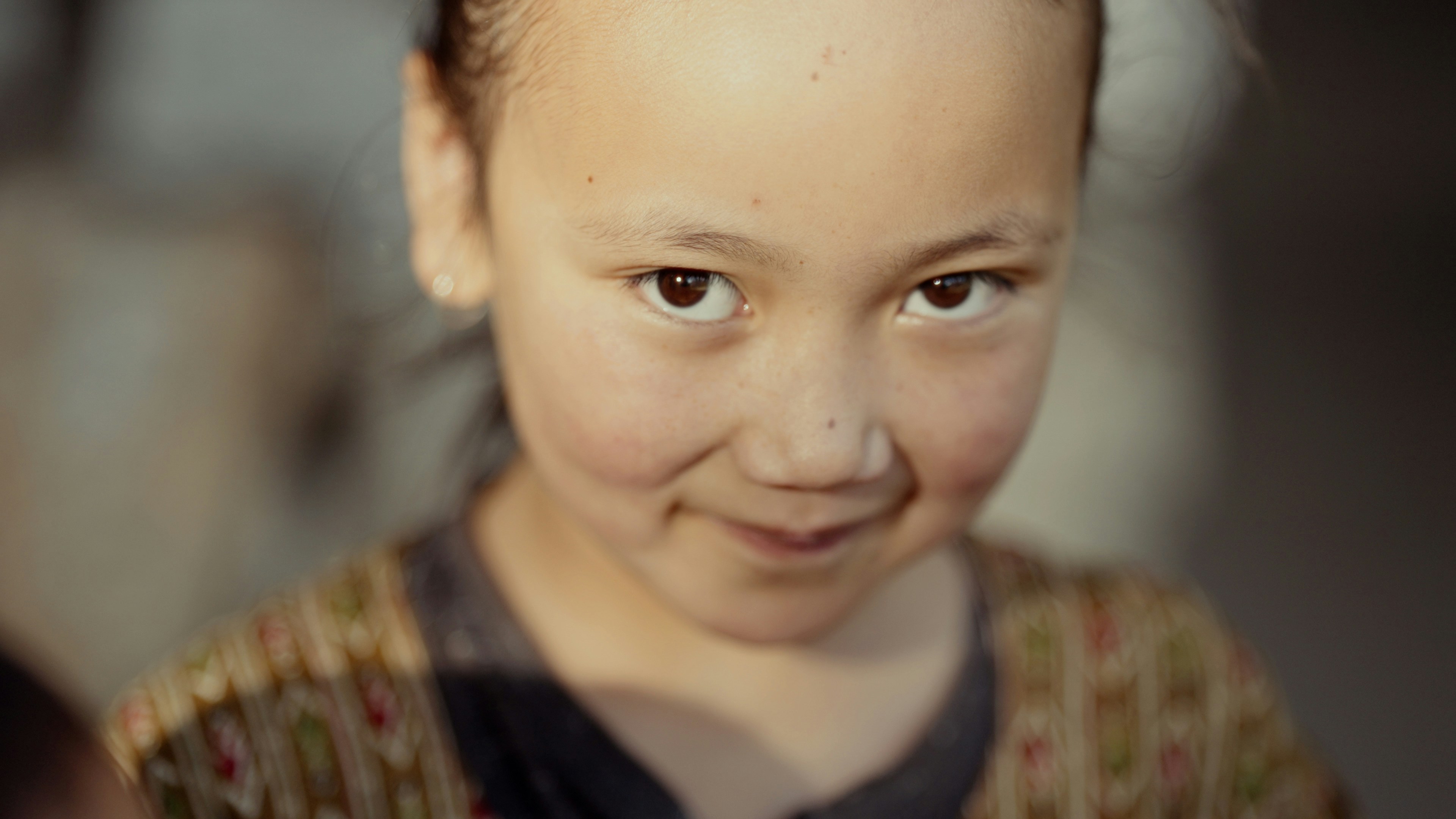 A young girl with a messy ponytail smiles at the camera