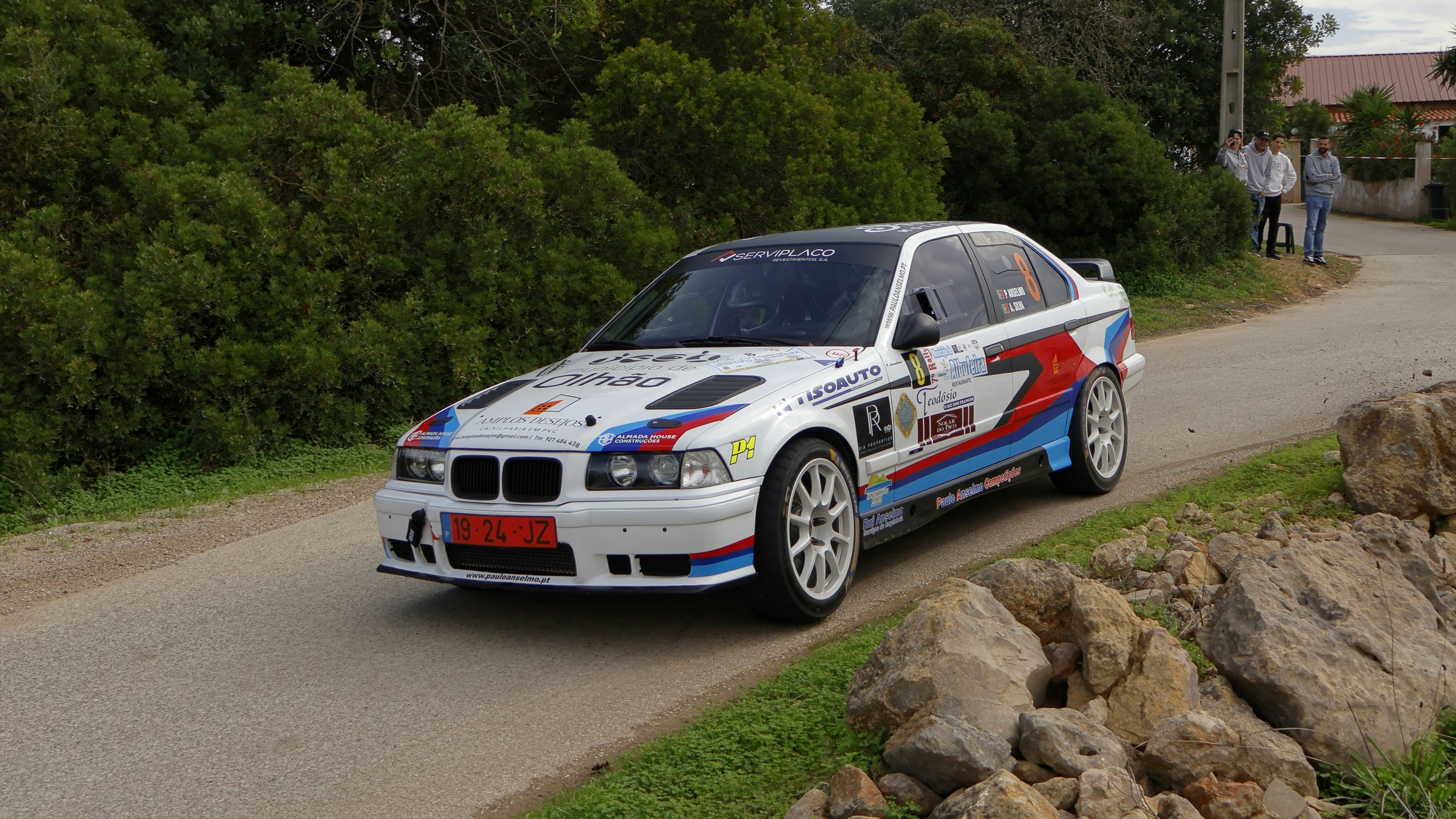 A white car driving down a street next to a lush green hillside