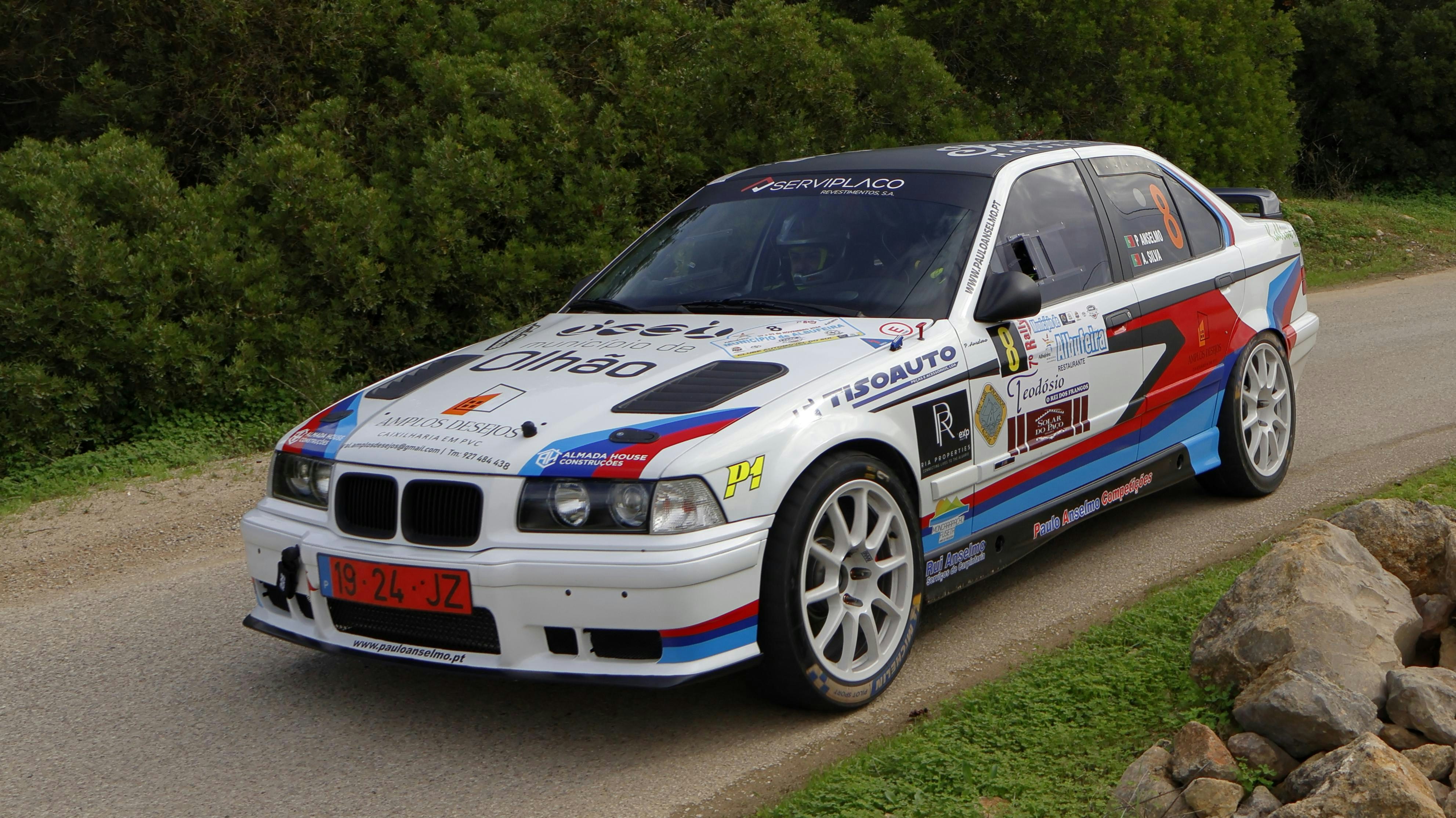 A white car driving down a road next to rocks