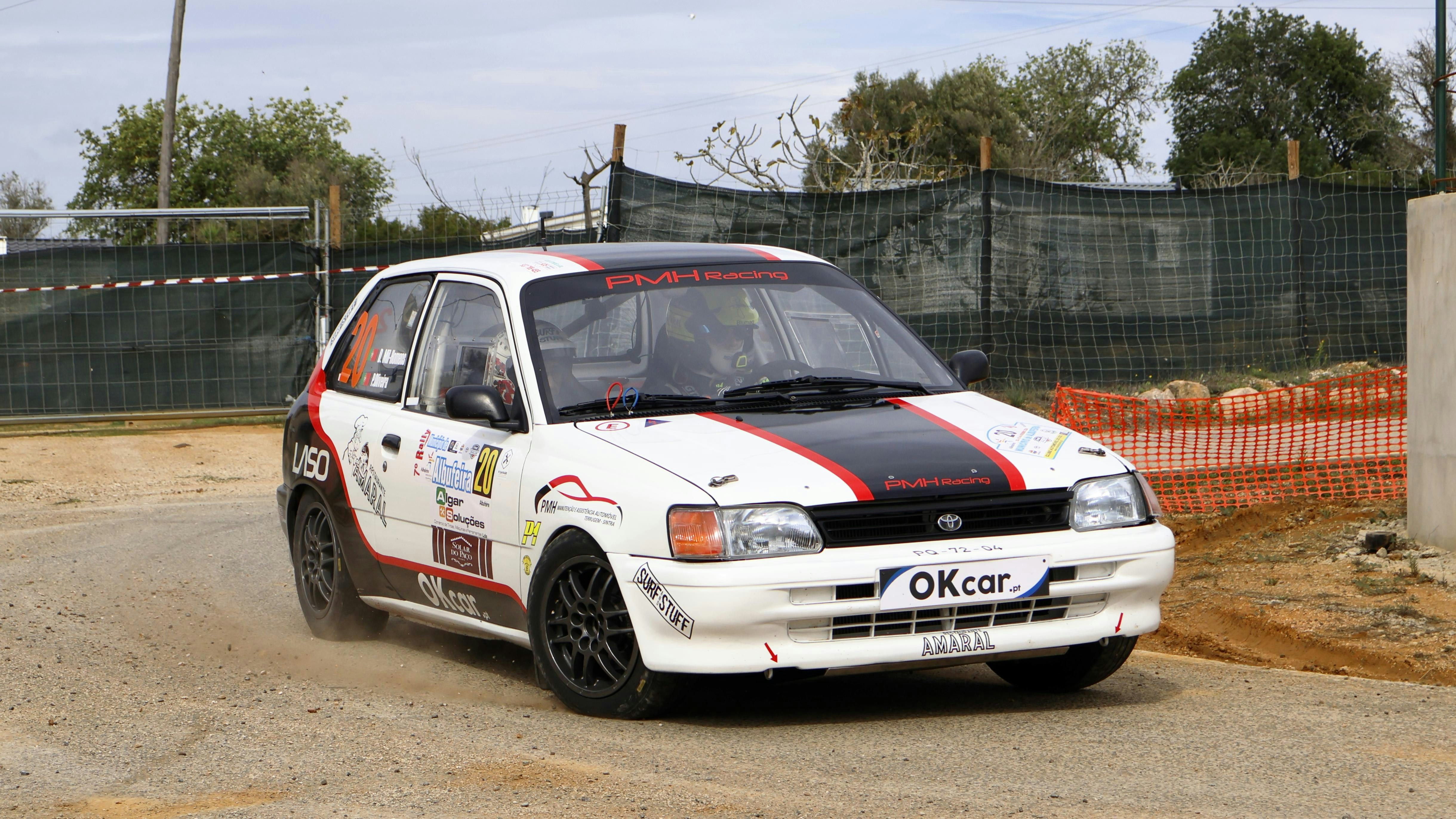 A small white car driving down a dirt road