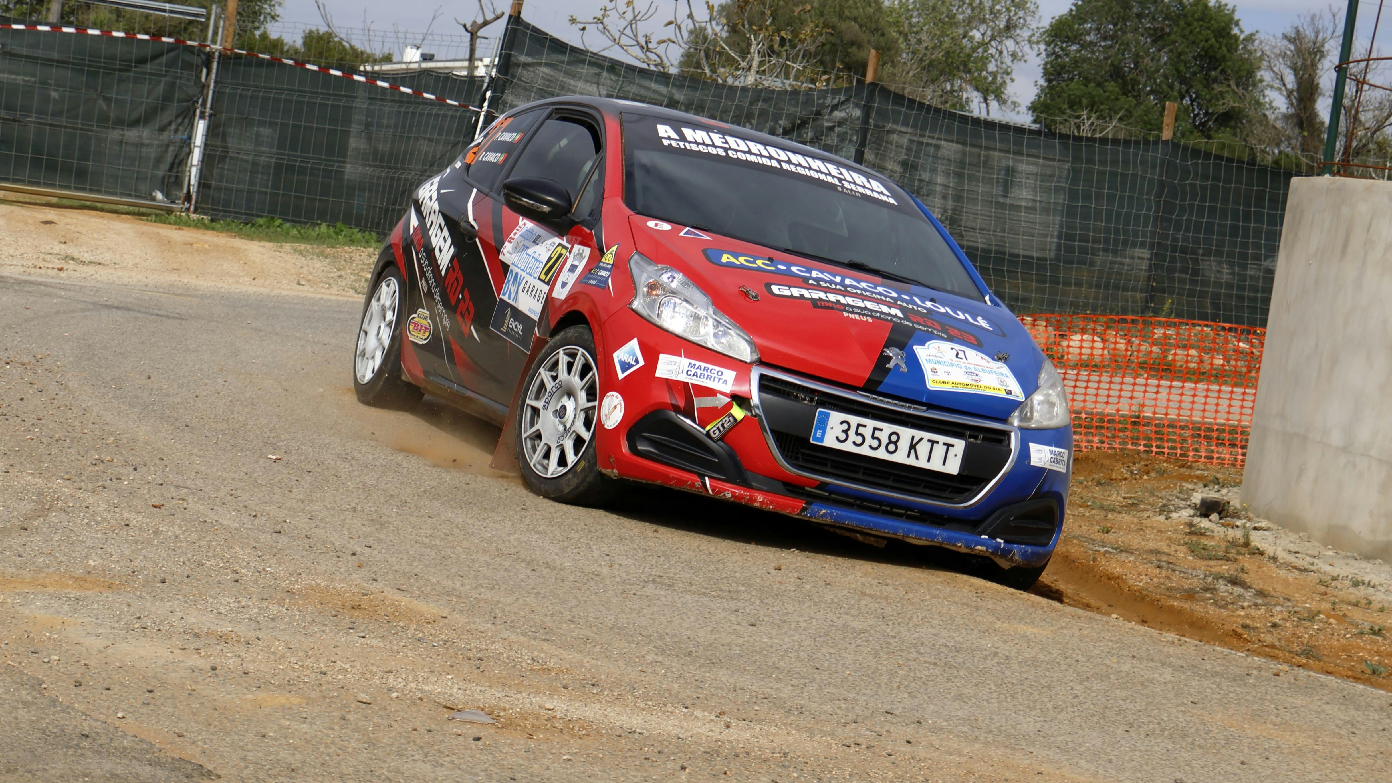 A red and blue car driving down a dirt road