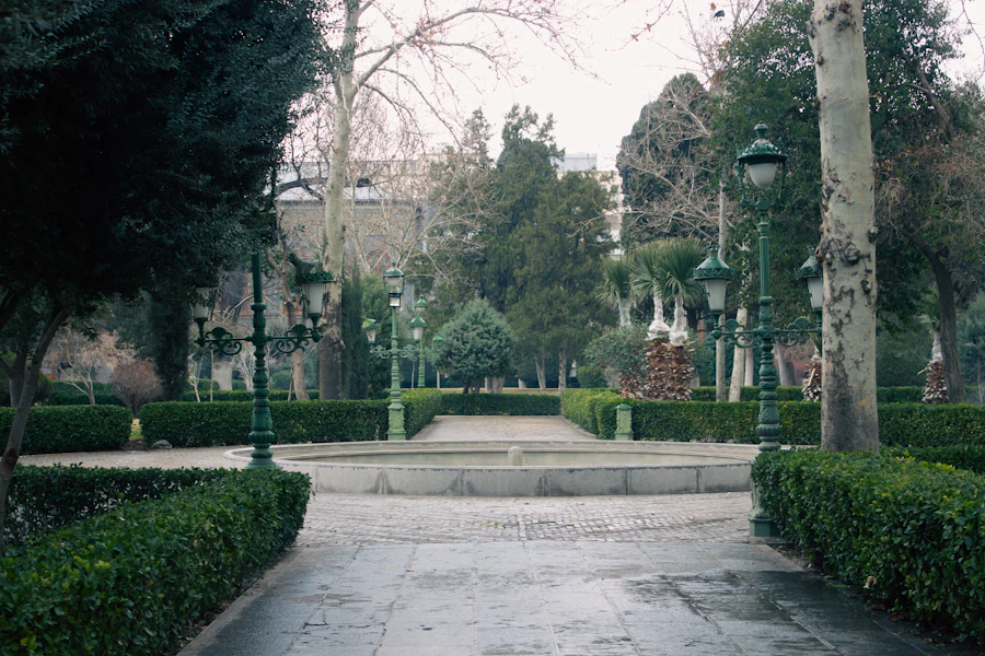 Public park with clipped hedging, stone paving, lamp posts and a canopy of mature trees