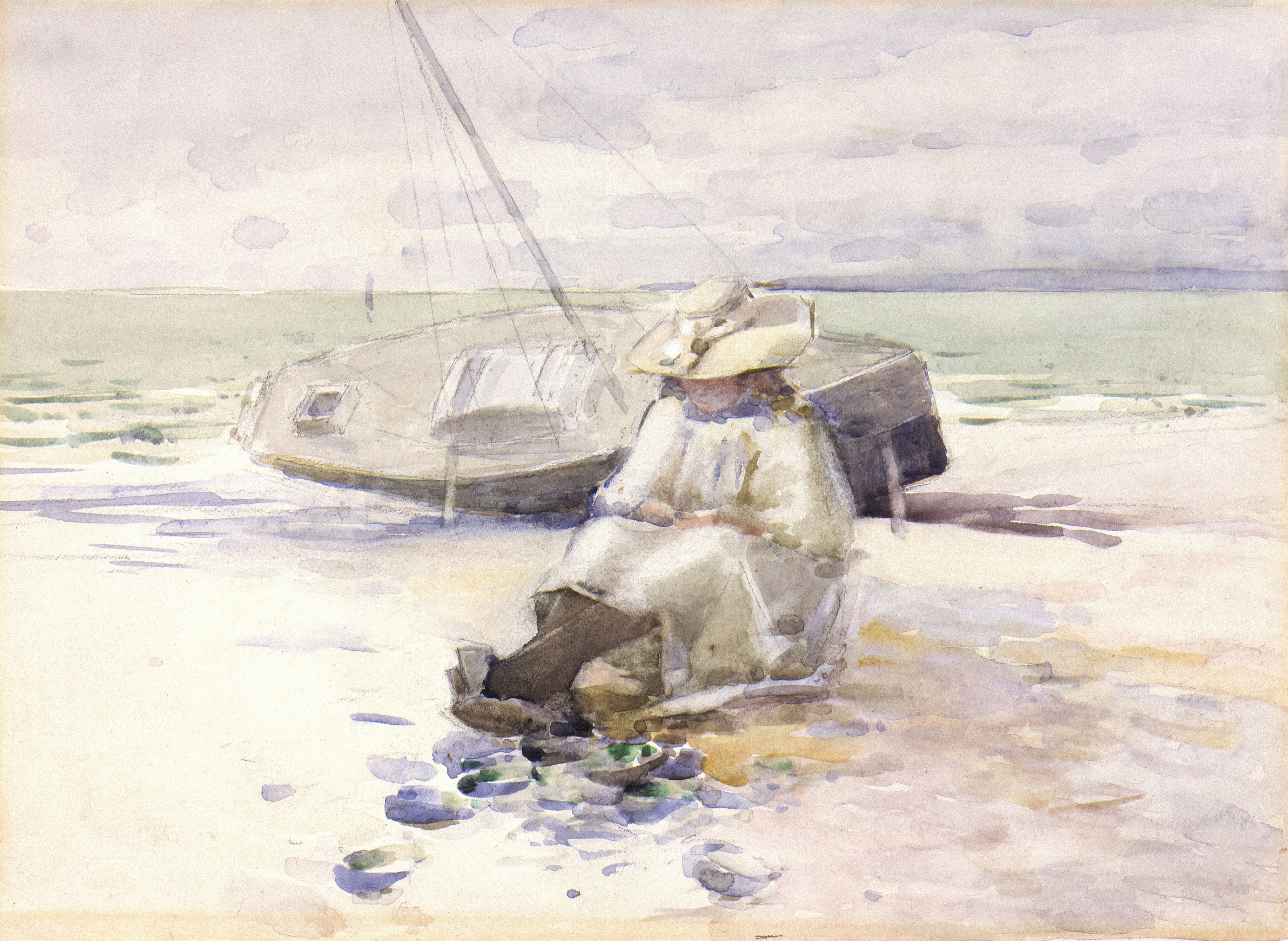 Woman sits on a beach near overturned boats.