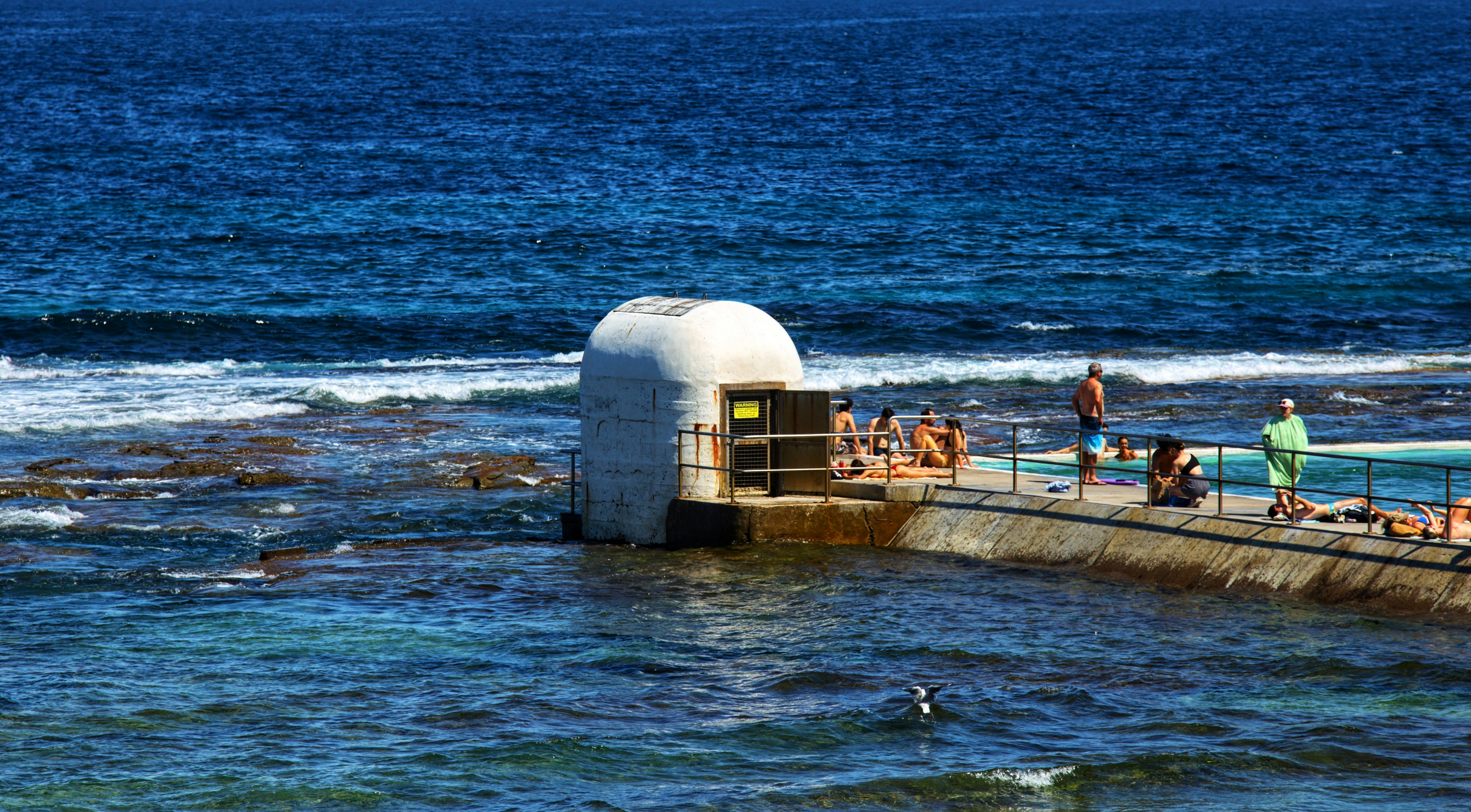 A group of people standing on a pier next to the ocean