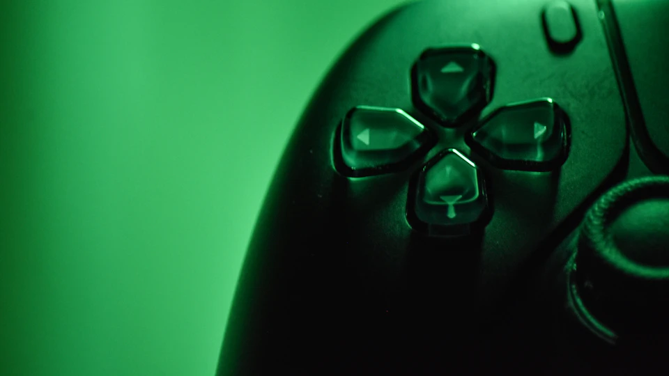 The image shows a close-up view of a black video game controller with four circular buttons arranged in a square pattern, each adorned with a small green gemstone at its center. The buttons are positioned on the right side of the controller and appear to be in good condition.
