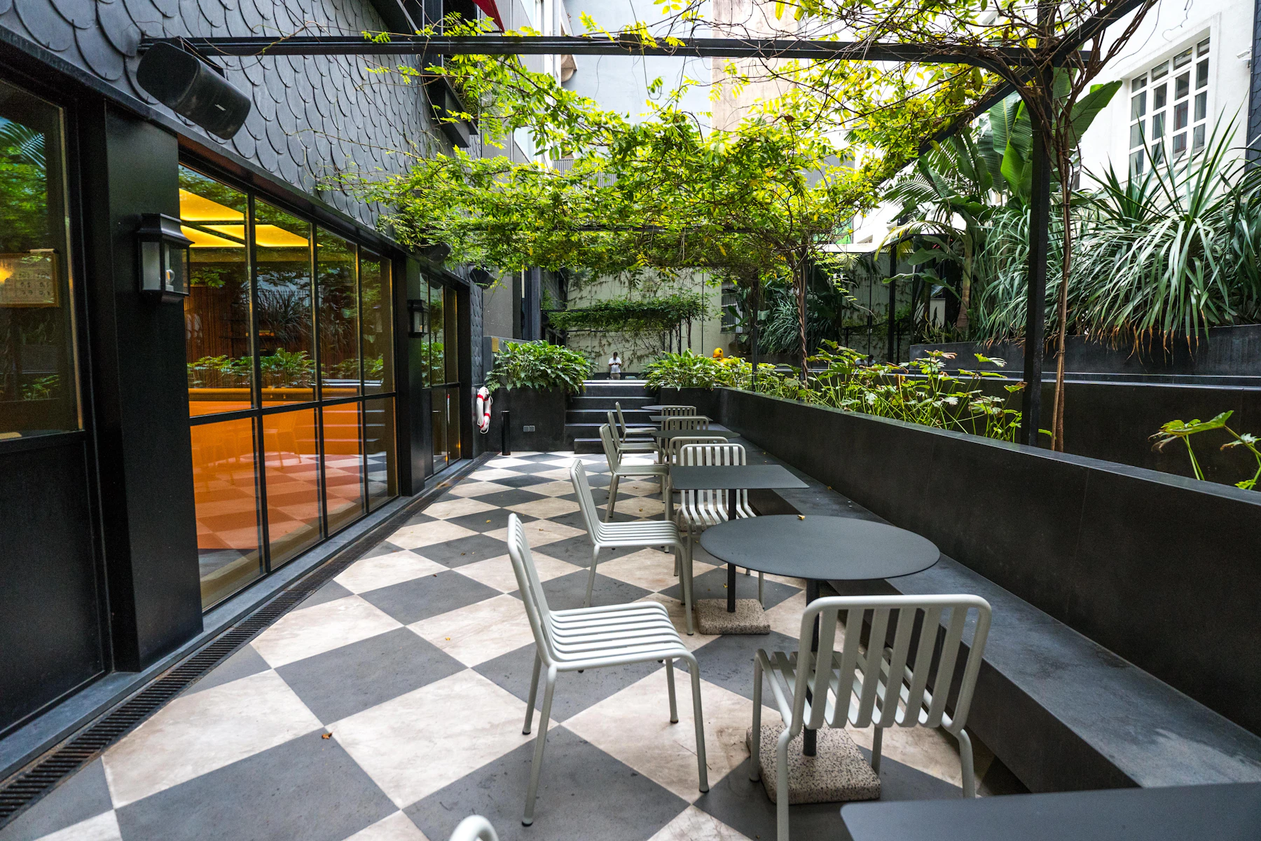 A long stone dining terrace with paired tables and chairs set against a clipped hedge