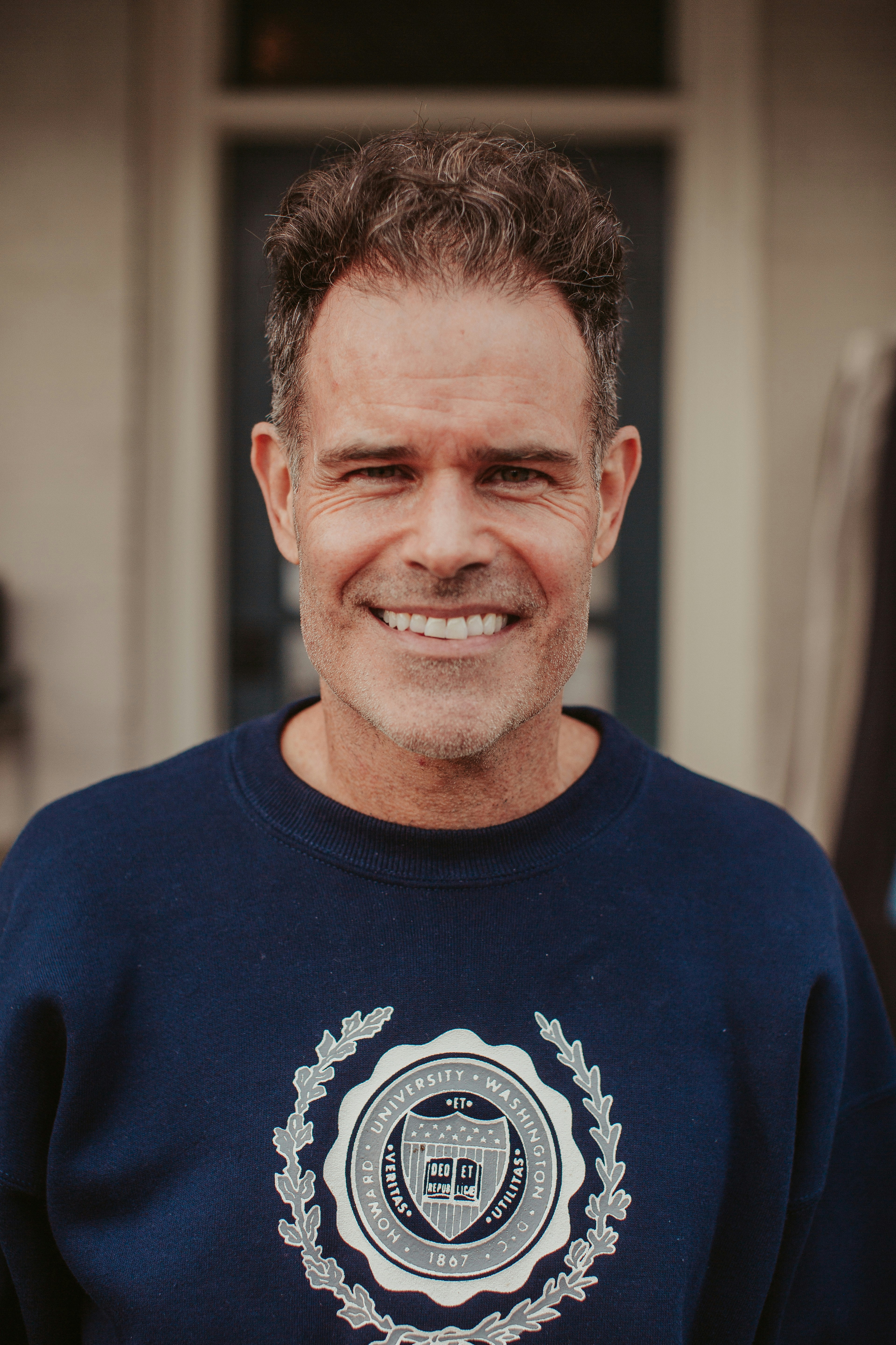 A smiling man in a blue sweatshirt stands in front of a door
