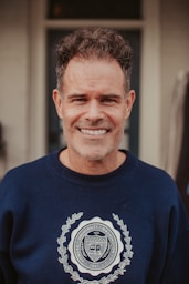 A smiling man in a blue sweatshirt stands in front of a door