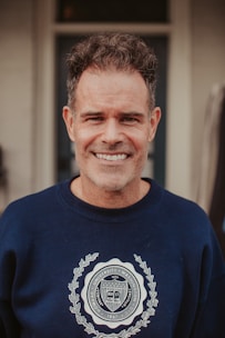 A smiling man in a blue sweatshirt stands in front of a door
