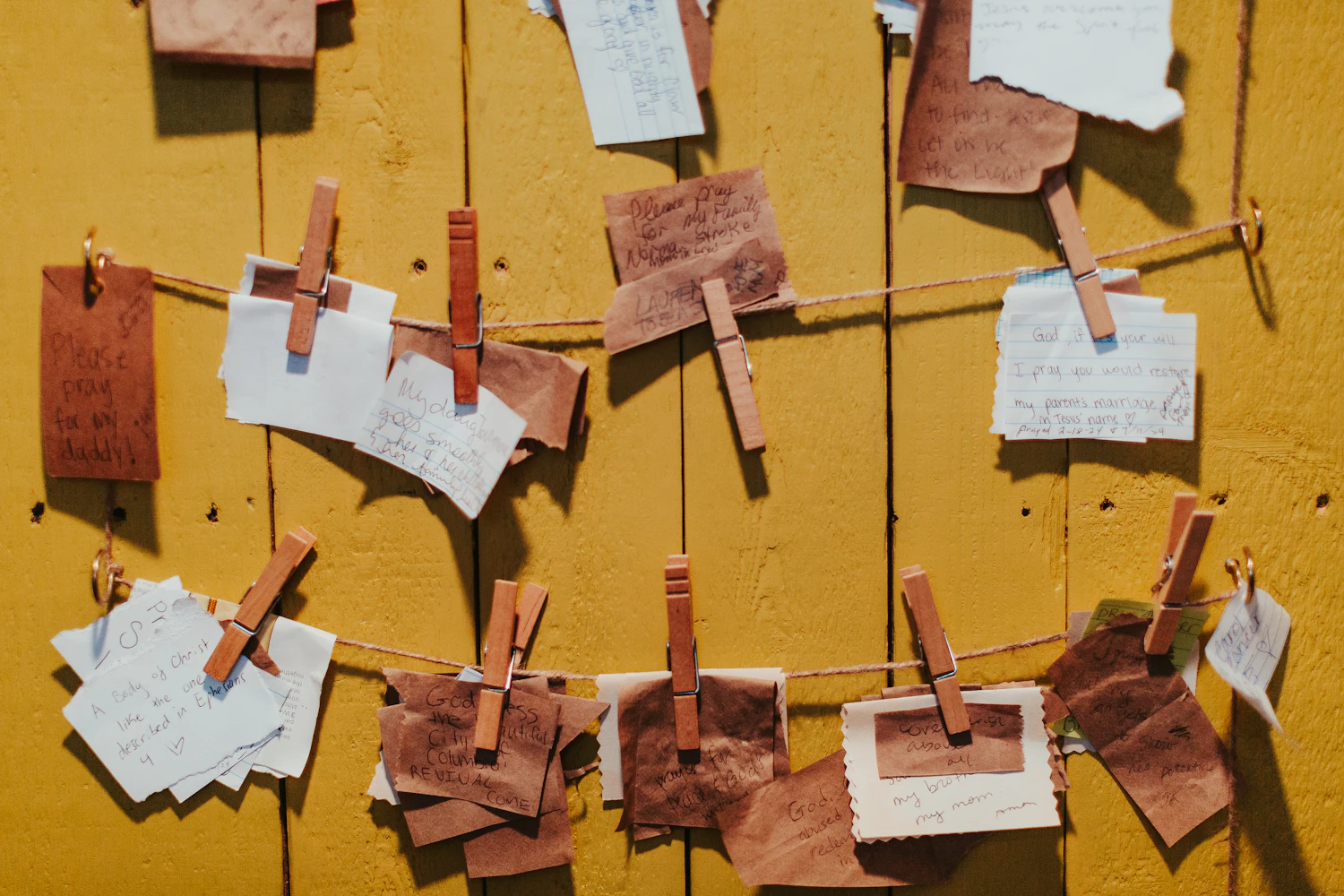 Scraps of paper and cloth pegged to two lines of twine across a yellow painted wall