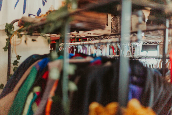 A rack of clothes in a store with a clock in the background