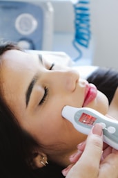 A woman laying in bed with a thermometer in her mouth