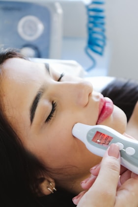 A woman laying in bed with a thermometer in her mouth
