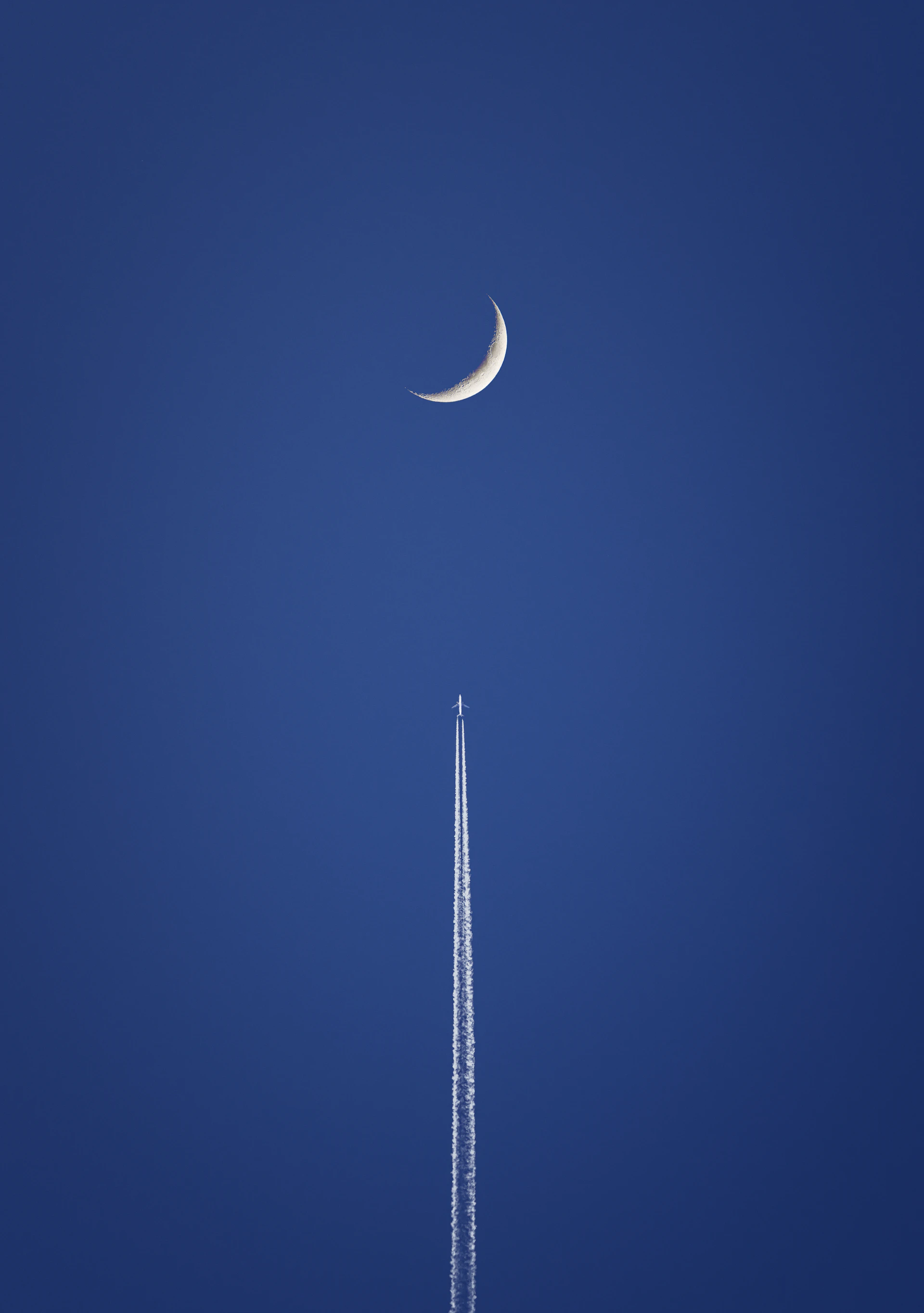 A plane flying in the sky with a crescent in the background
