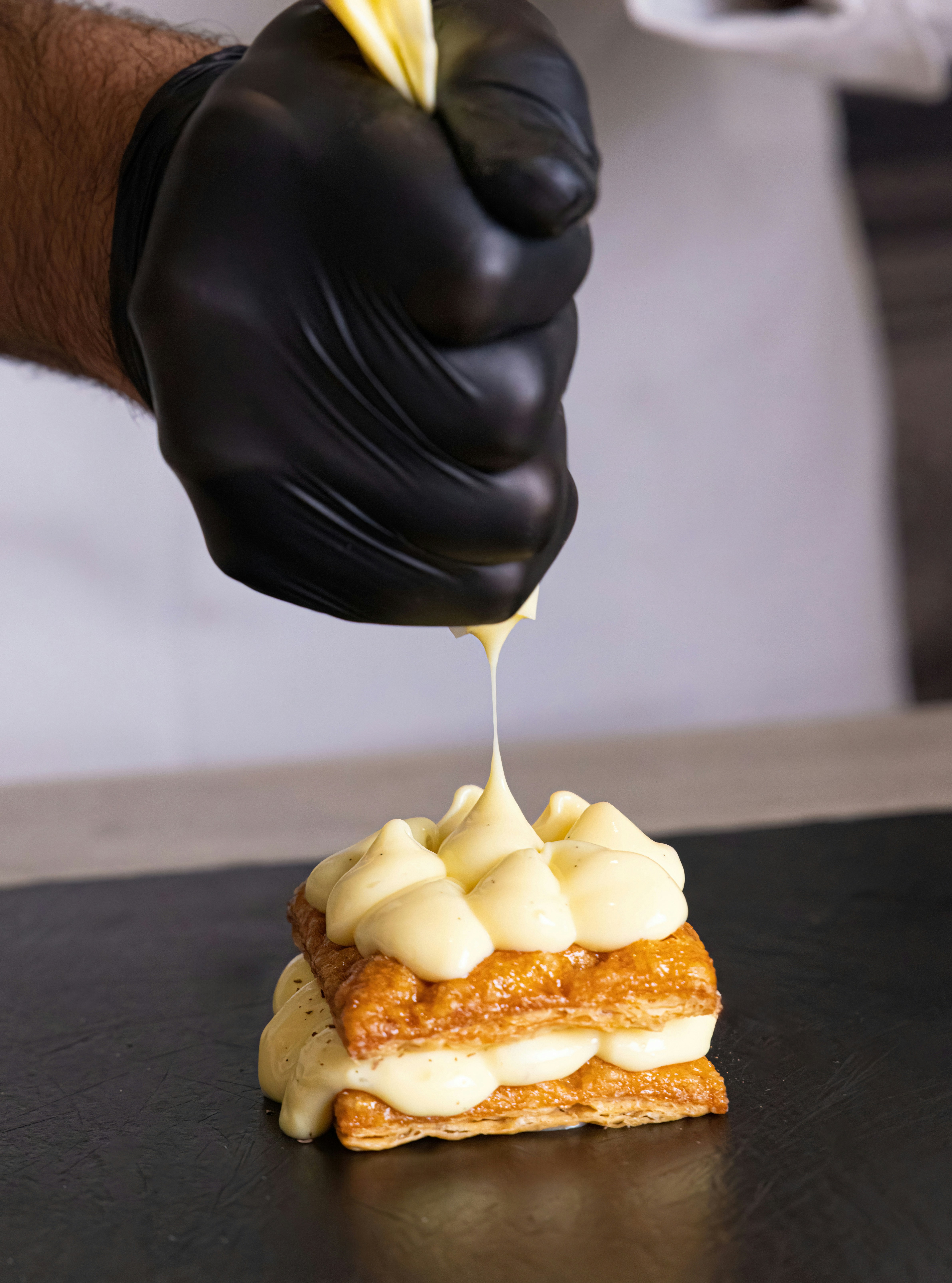 A person in black gloves drizzling icing onto a piece of cake