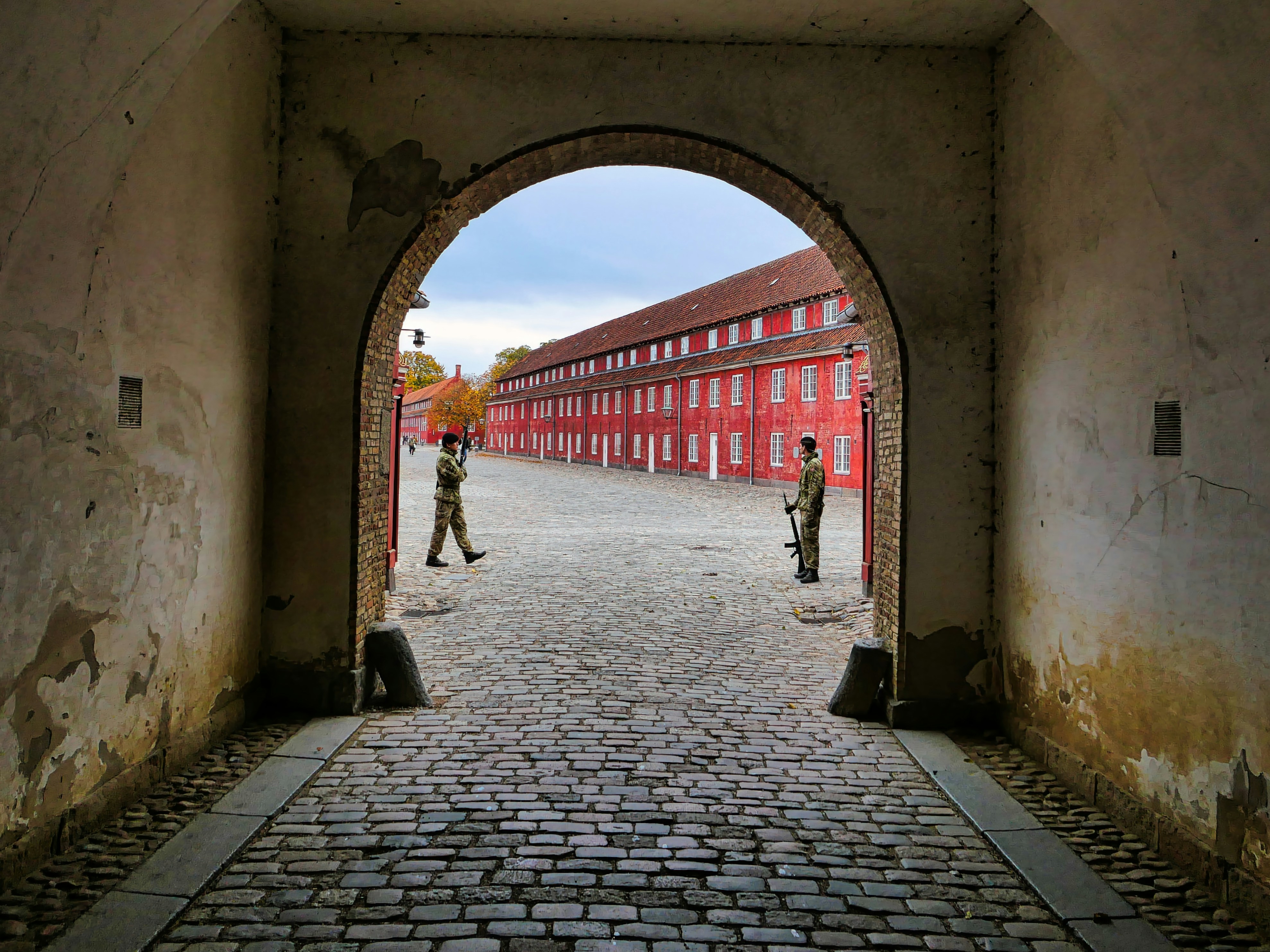 A man walking through a tunnel with a red building in the background