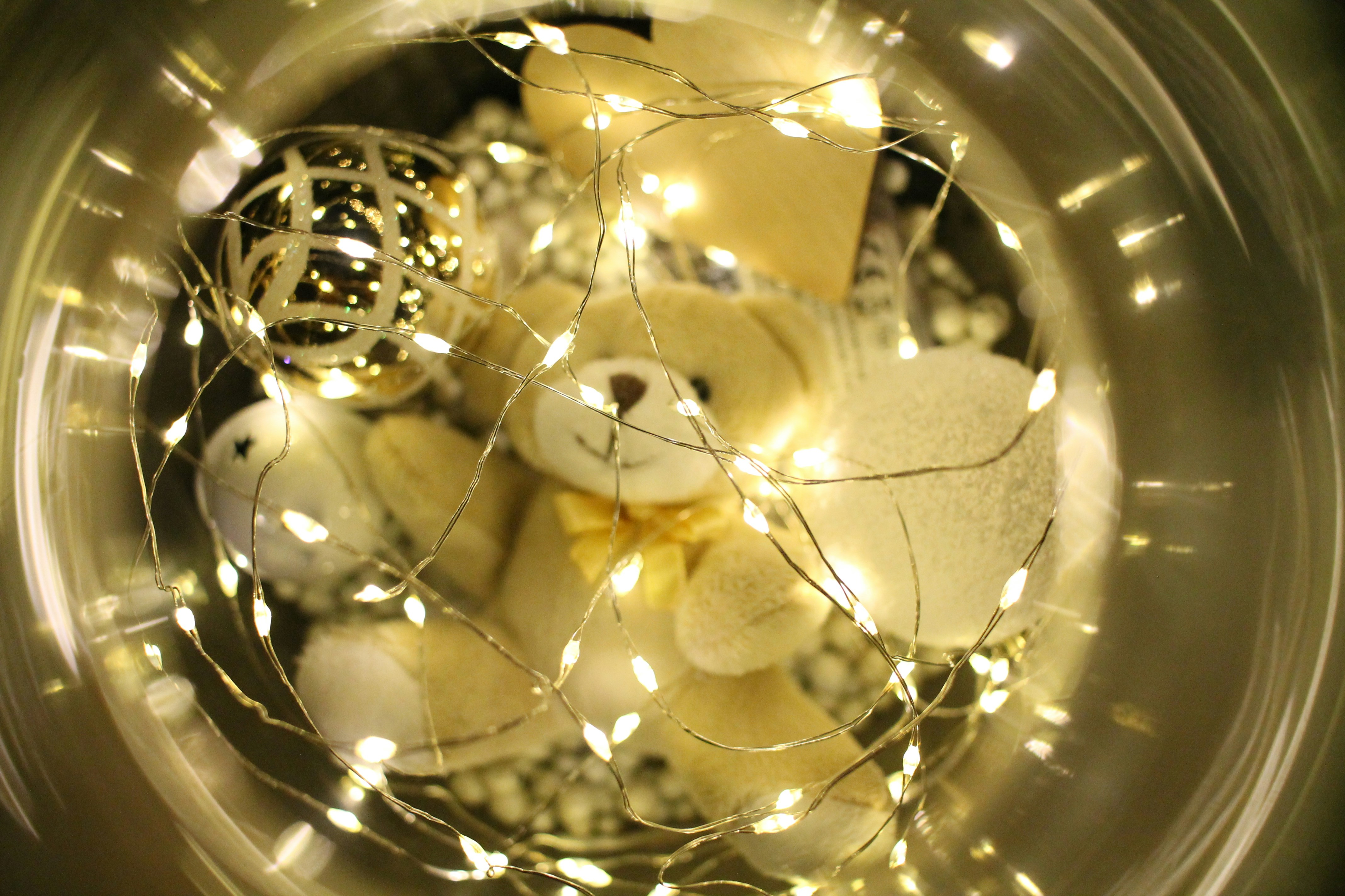 A teddy bear in a glass bowl with a string of lights