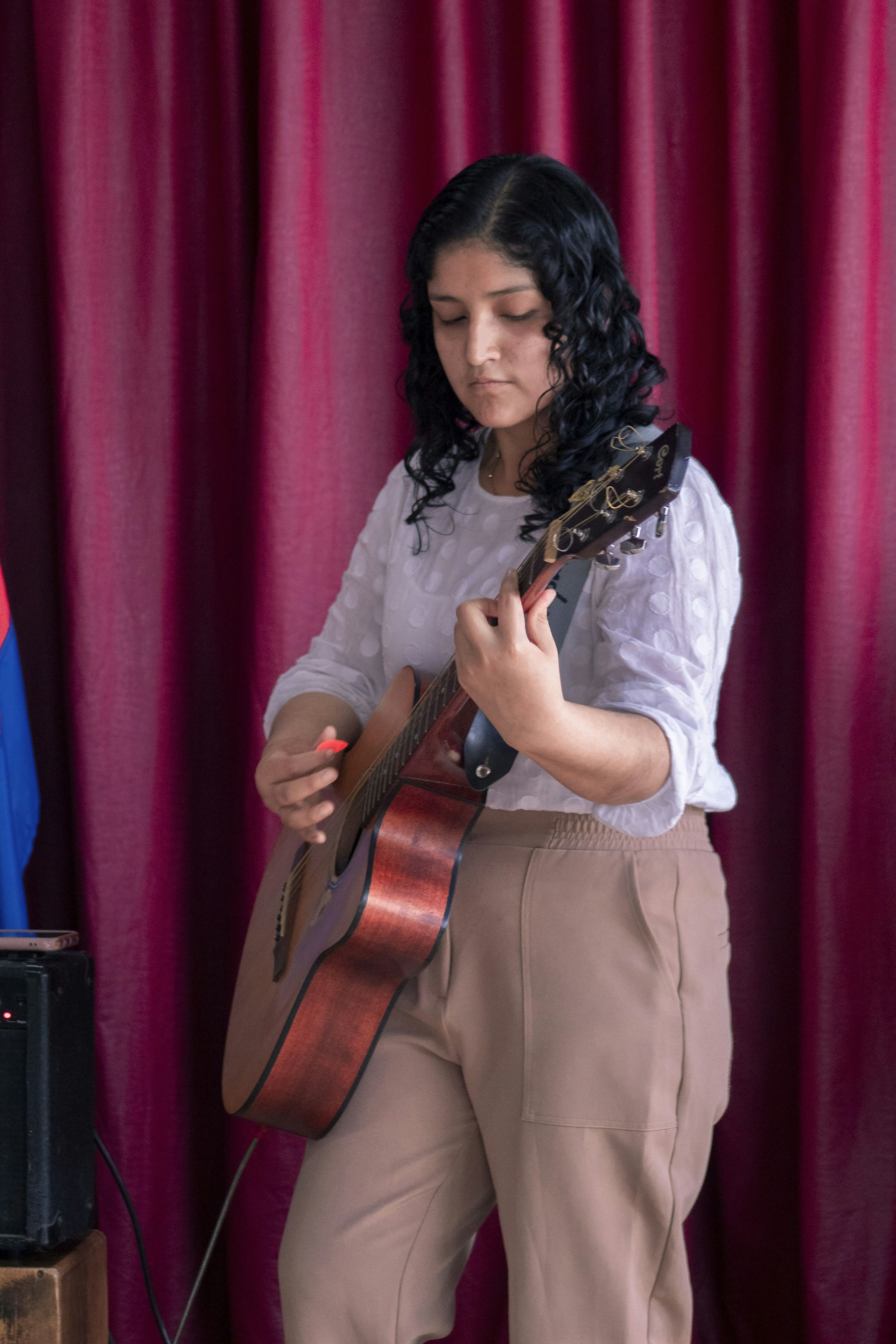 A woman playing a guitar in front of a red curtain