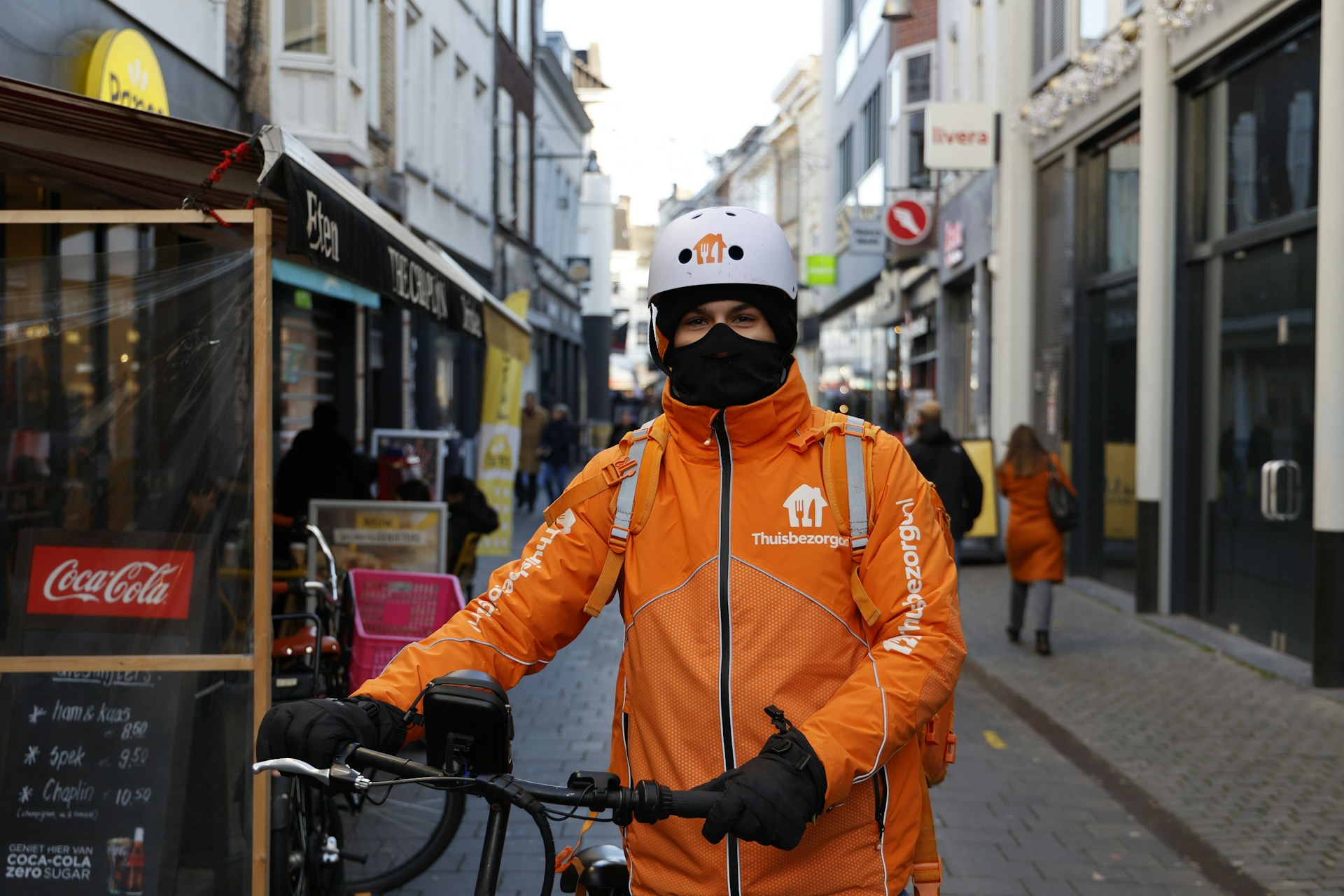 A man in an orange jacket is holding a bicycle