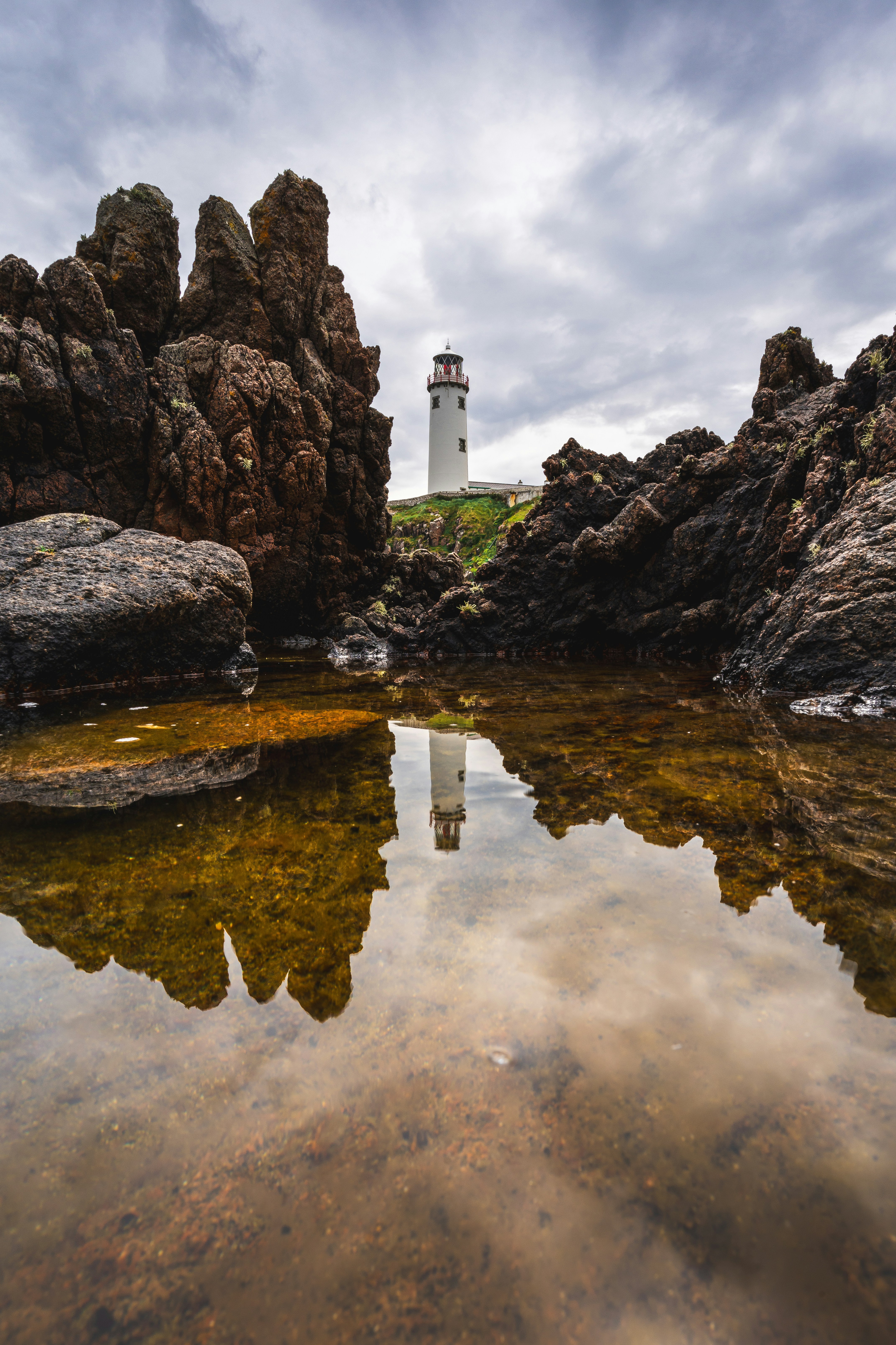 A lighthouse on a rocky shore near a body of water photo – Free Photo ...