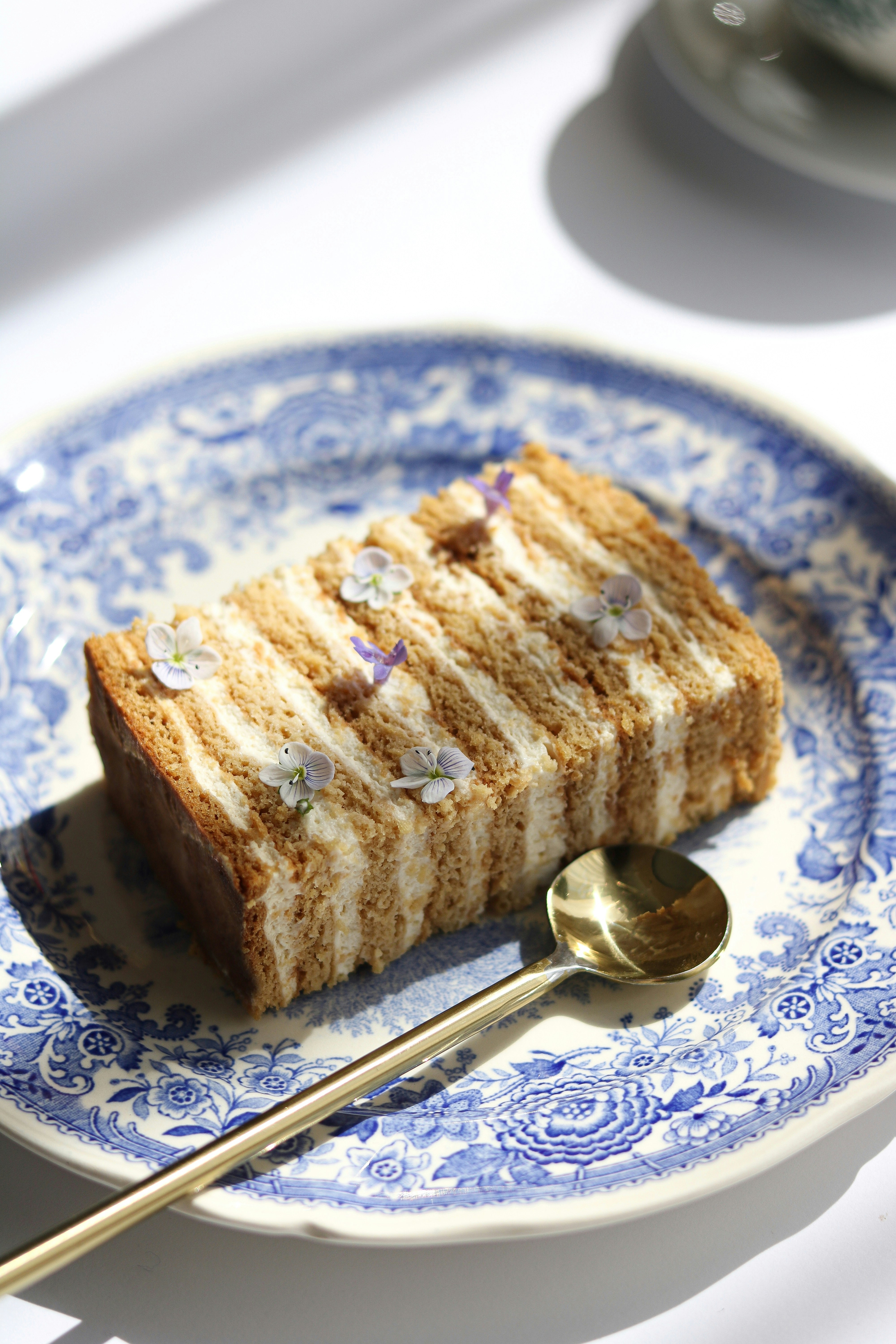 Elegant layered lavender cake slice with cream frosting and dried flowers on a white plate