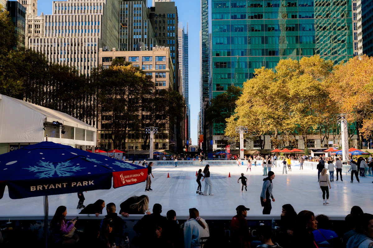 Skaters on the Bryant Park rink in daylight with Midtown towers behind