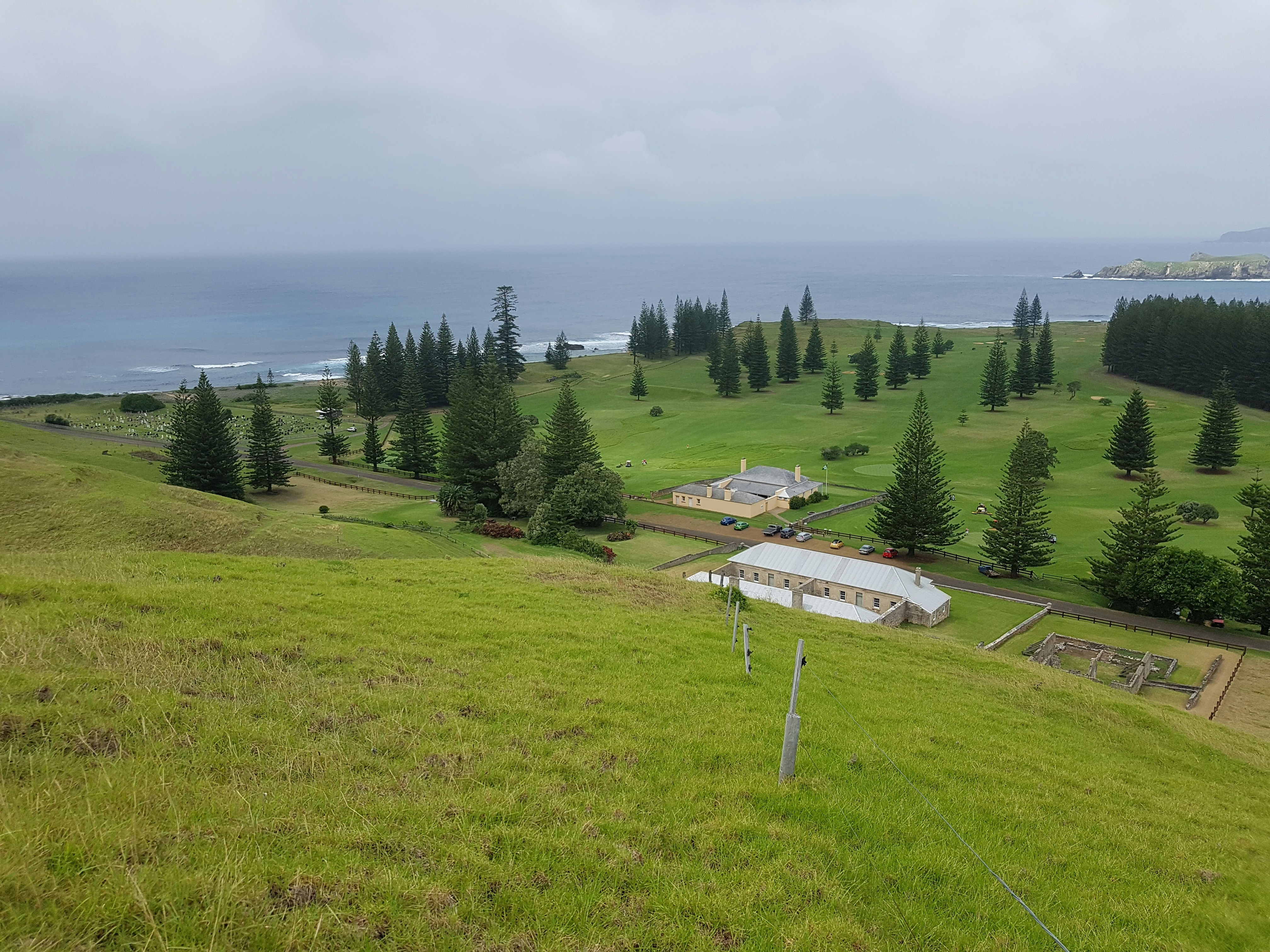 A grassy field with a farm and a body of water in the distance