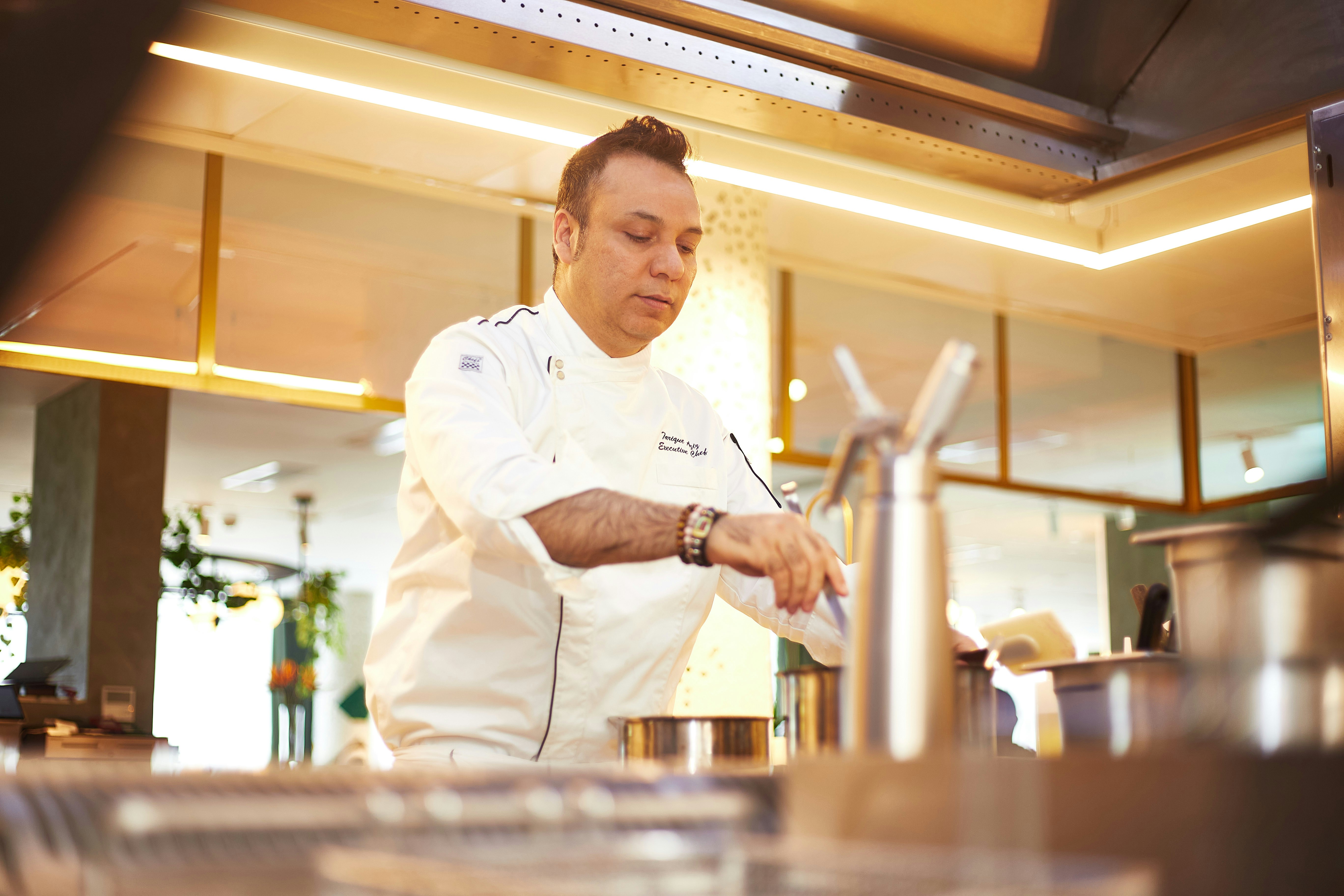 Executive chef in white chef coat with focused expression, professional kitchen background with warm ambient lighting