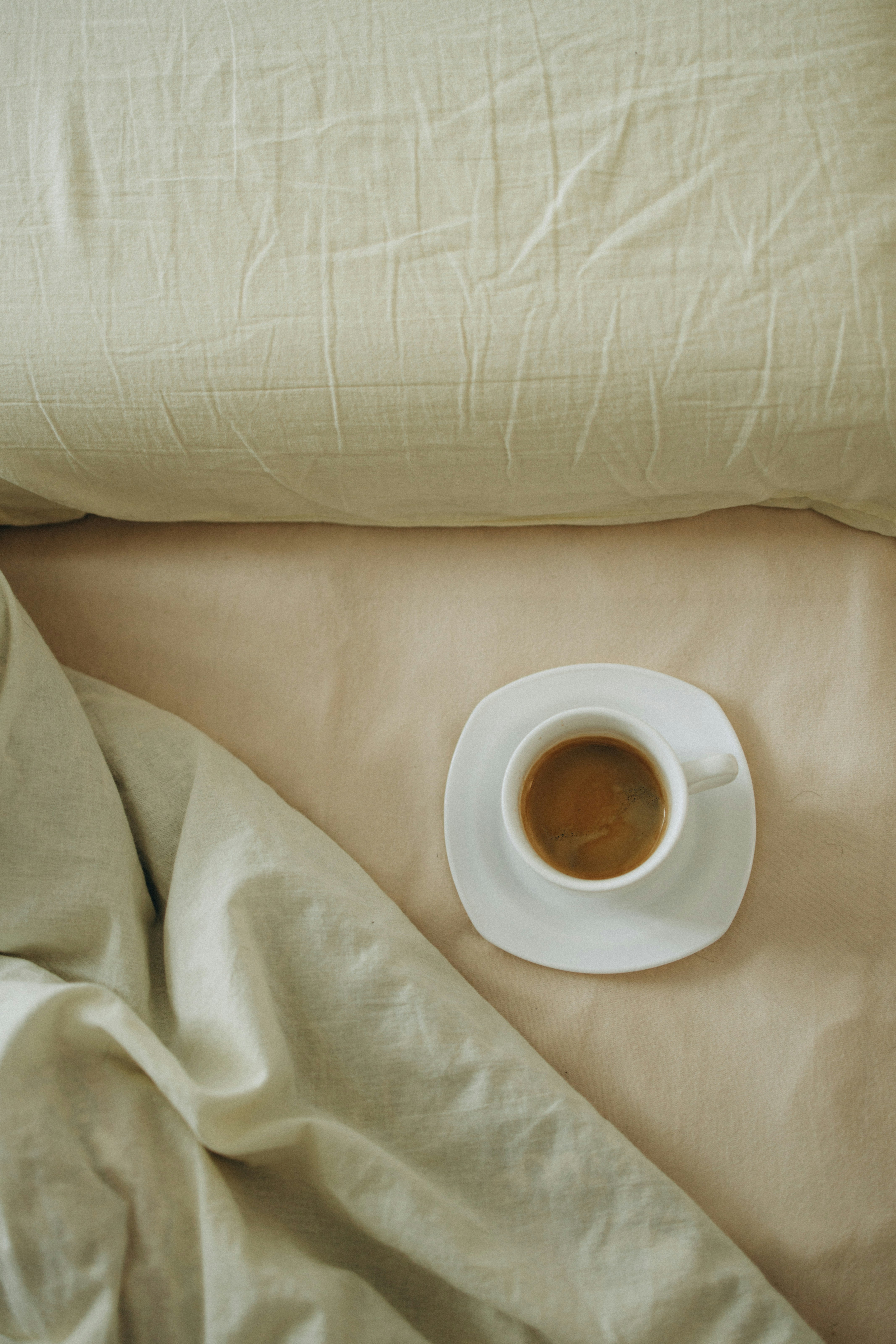 A cup of coffee sitting on top of a bed next to a pillow