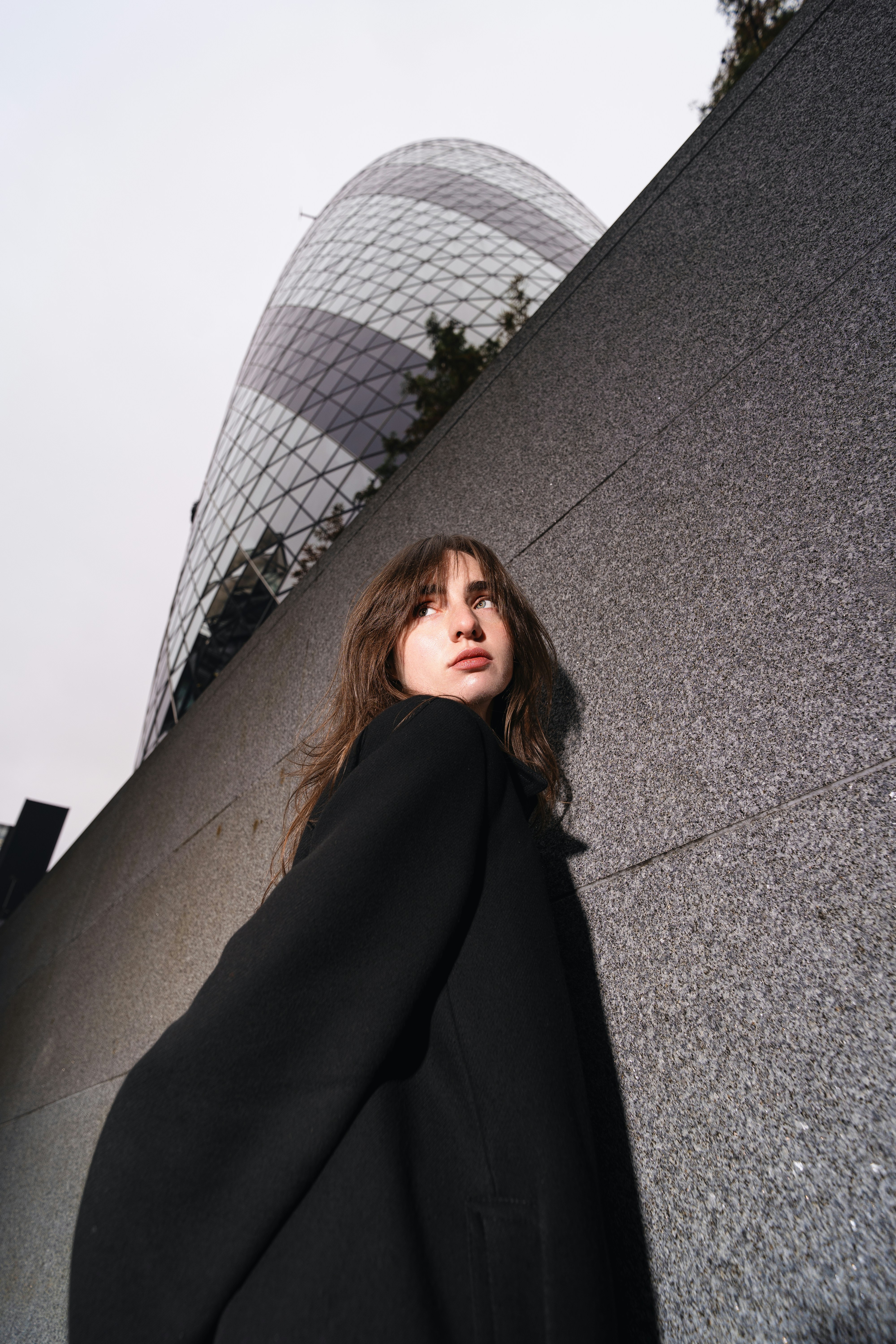 A woman leaning against a wall with a building in the background