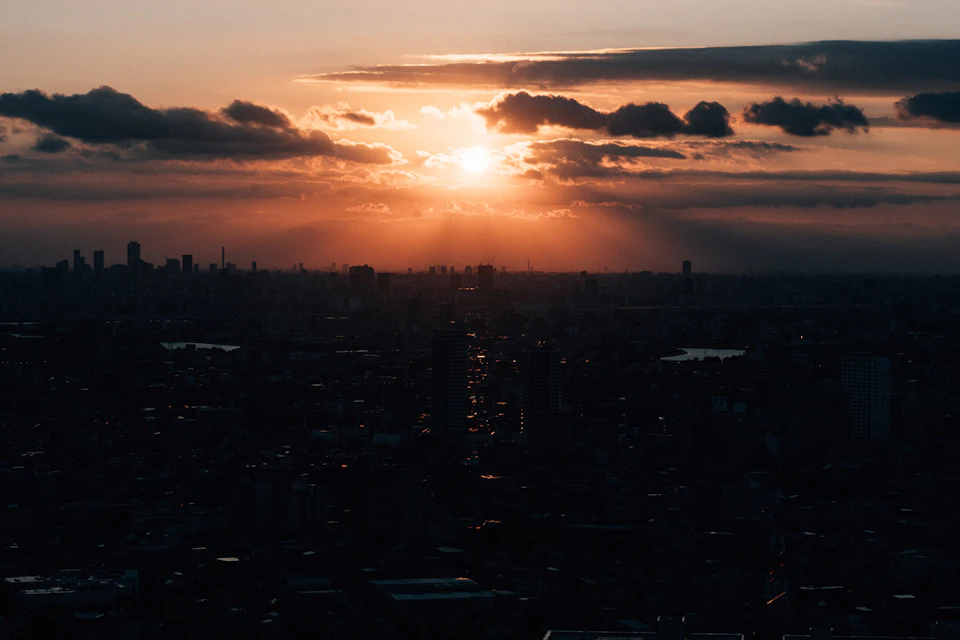 Cityscape at sunset with warm glow, dense clouds, and sprawling urban landscape in foreground