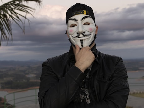 A man wearing a guy fappe mask with a palm tree in the background