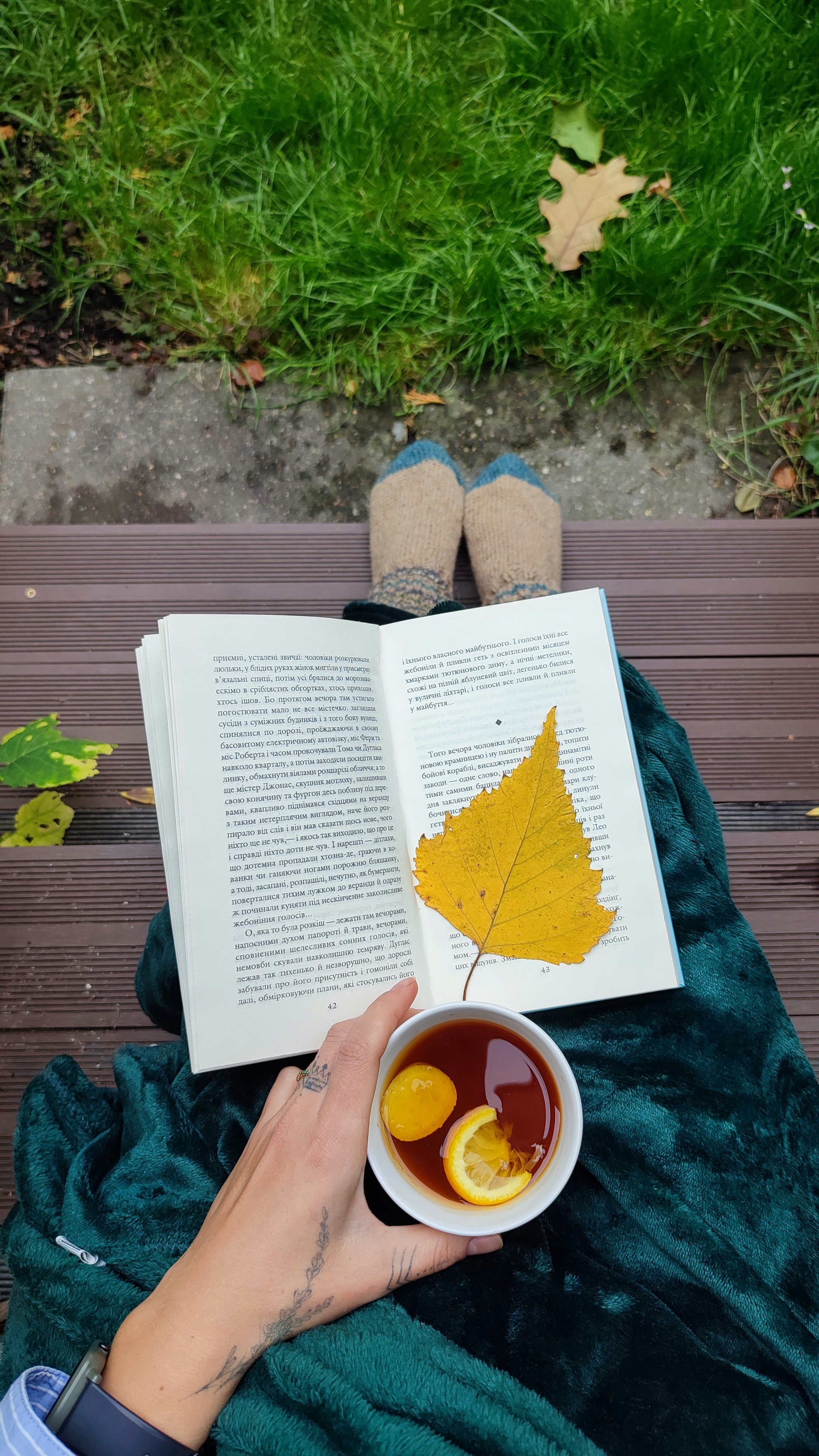 A person sitting on a bench reading a book and holding a bowl of fruit