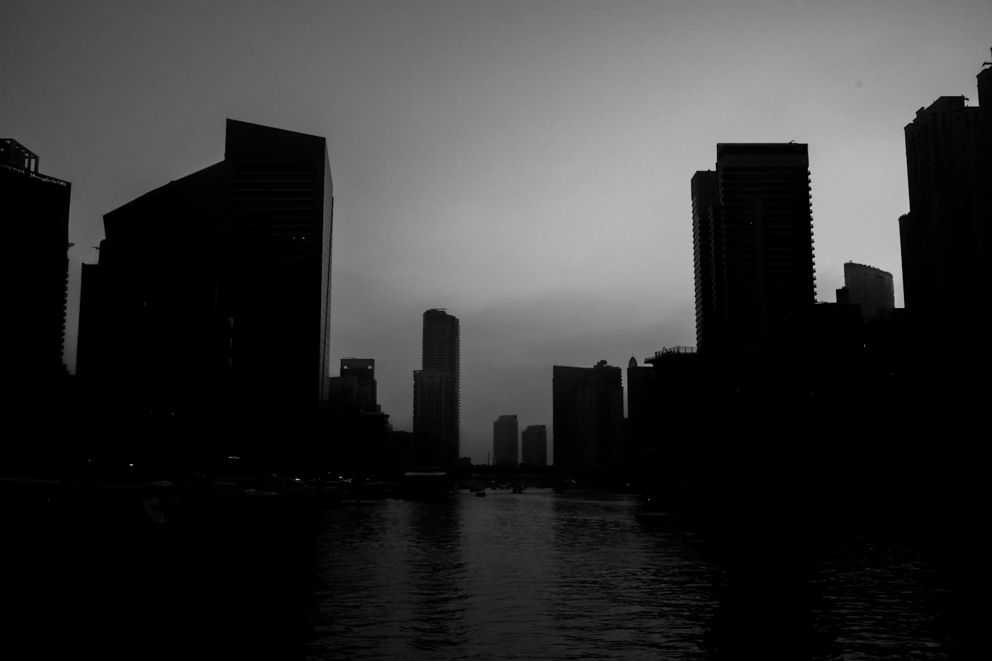 Silhouetted towers along a river at dusk, in black and white